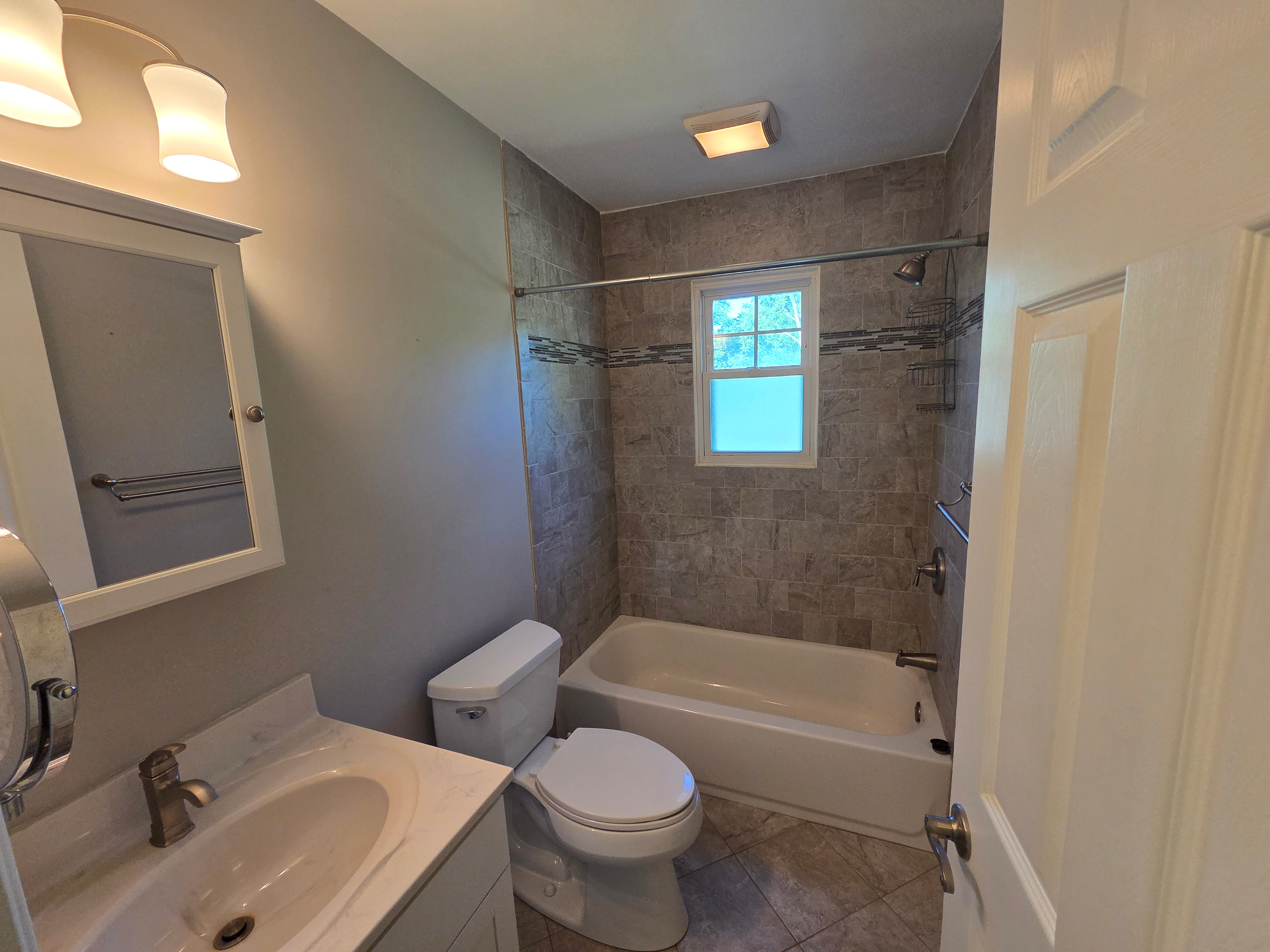 Renovated full bathroom with floor-to-ceiling tile work, white vanity, and silver hardware