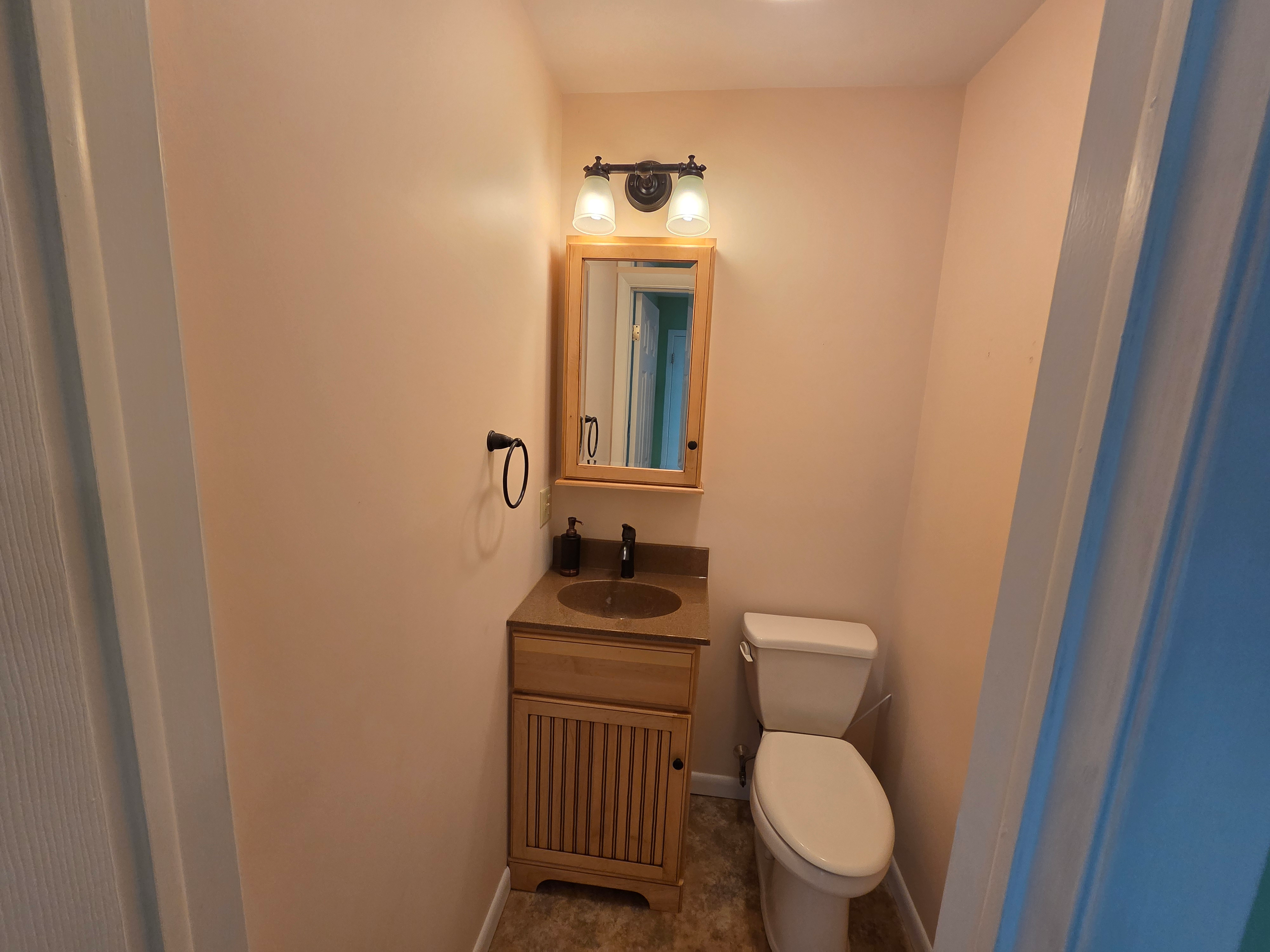 Half bathroom with light wood cabinetry, laminate vanity top, and beige wall paint