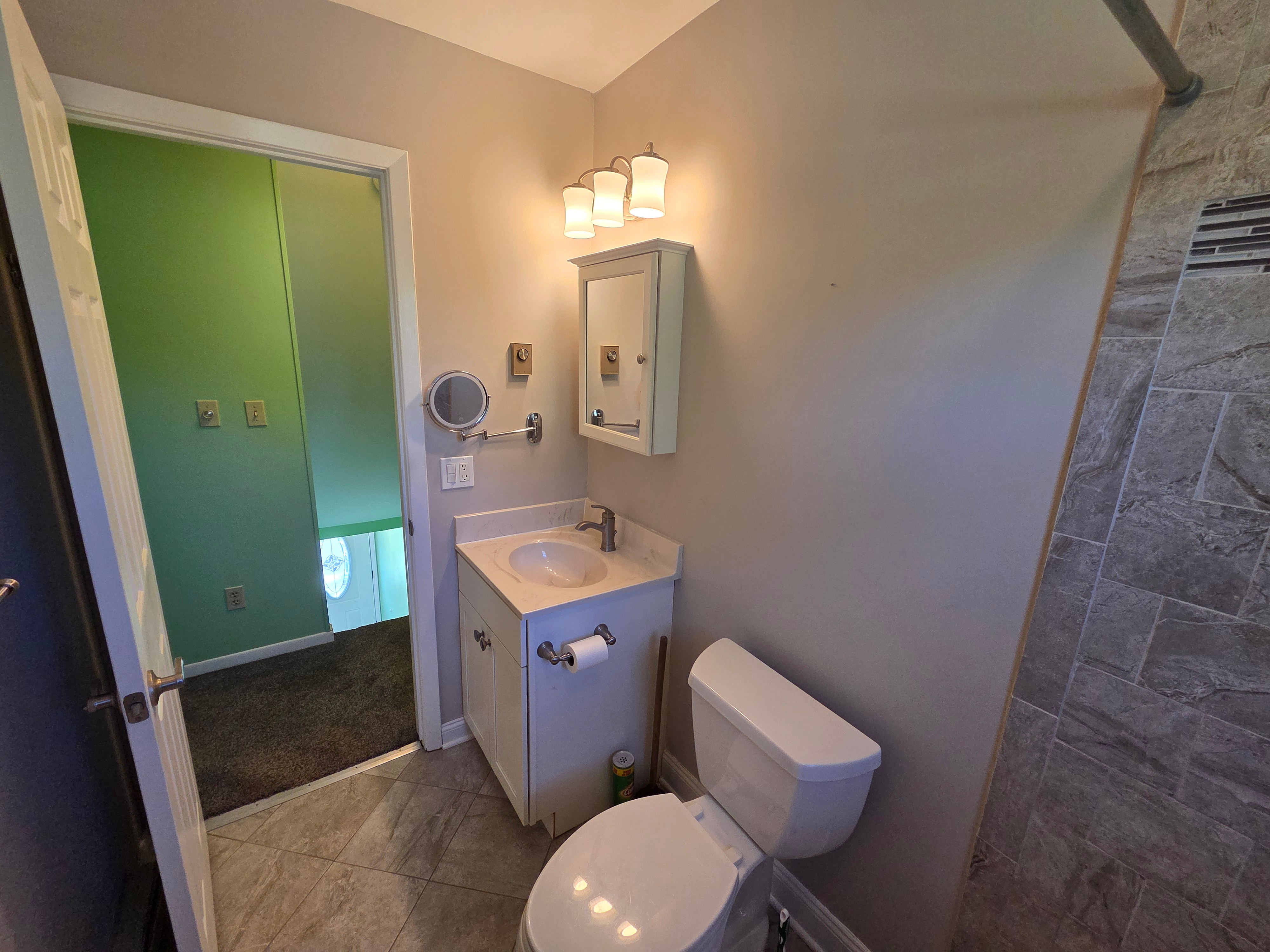 Remodeled bathroom with grey stone-look tile, white cabinetry, and modern vanity