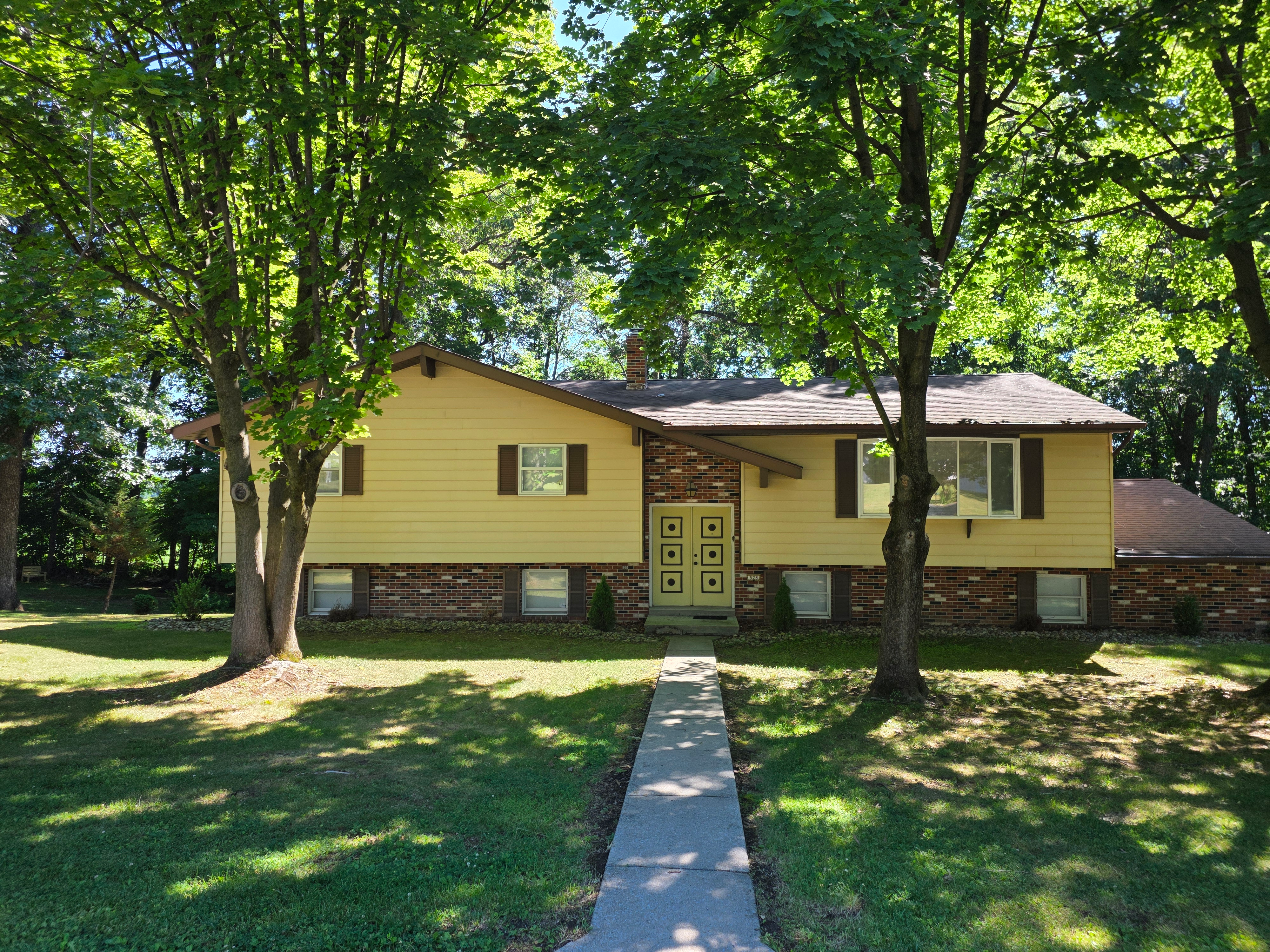 Front exterior of 528 Rosewood Dr, a bi-level home with beige siding and brick accents under mature trees