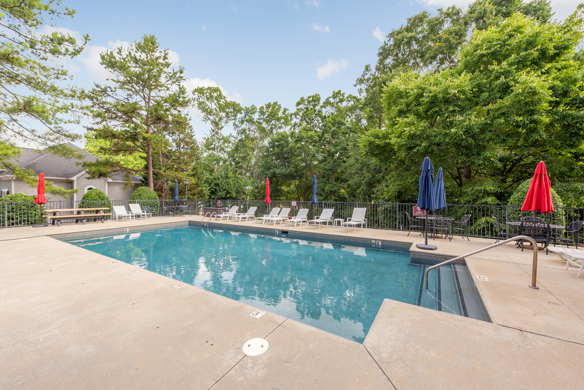 Community outdoor swimming pool with lounge chairs and umbrella-shaded bistro tables
