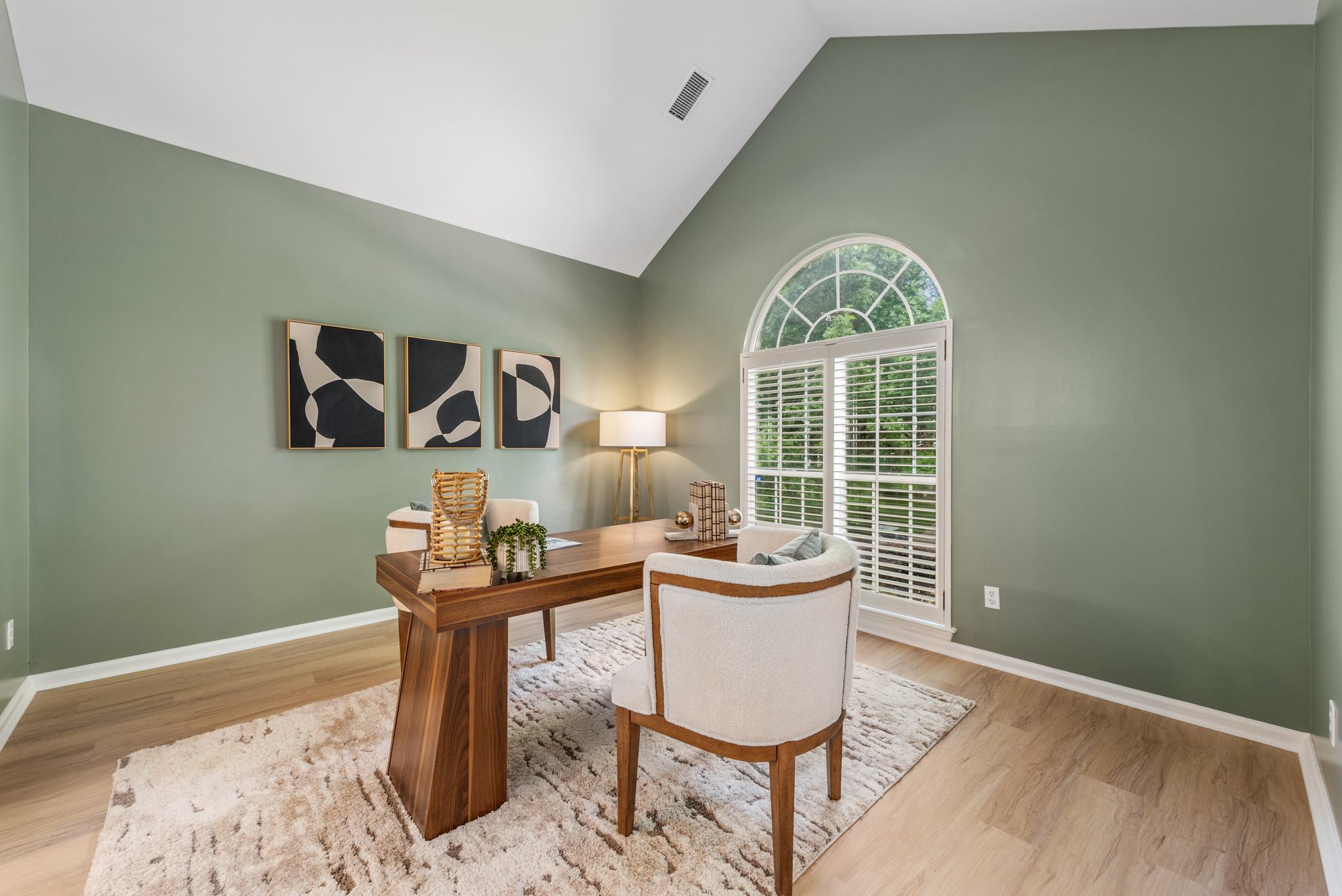 Private home office with vaulted ceiling, sage green walls, and plantation shutters