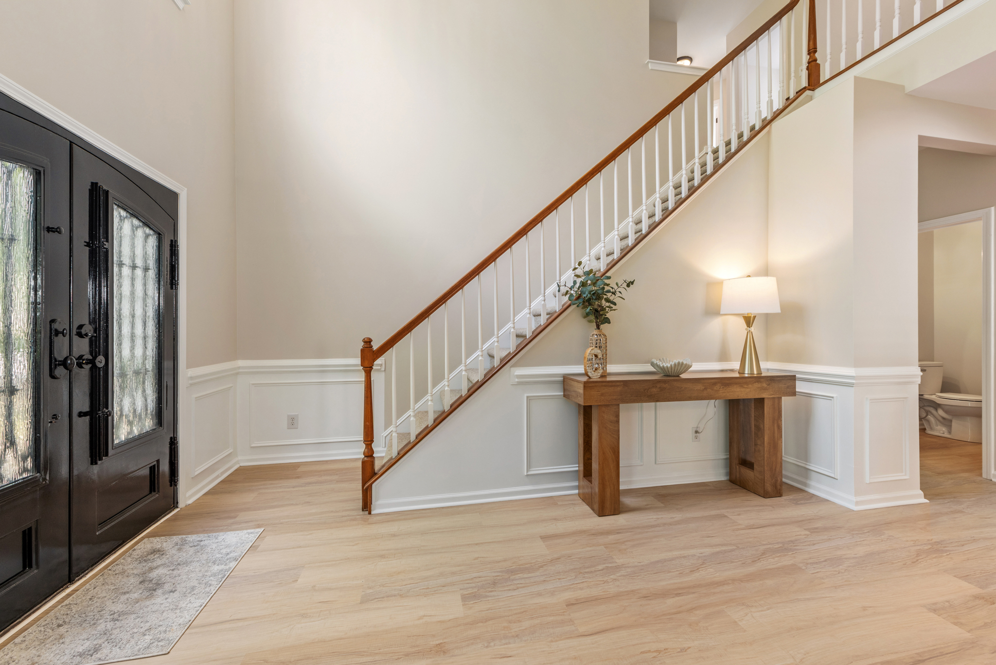 Grand foyer with light wood flooring, wainscoting, and dark double-door entrance