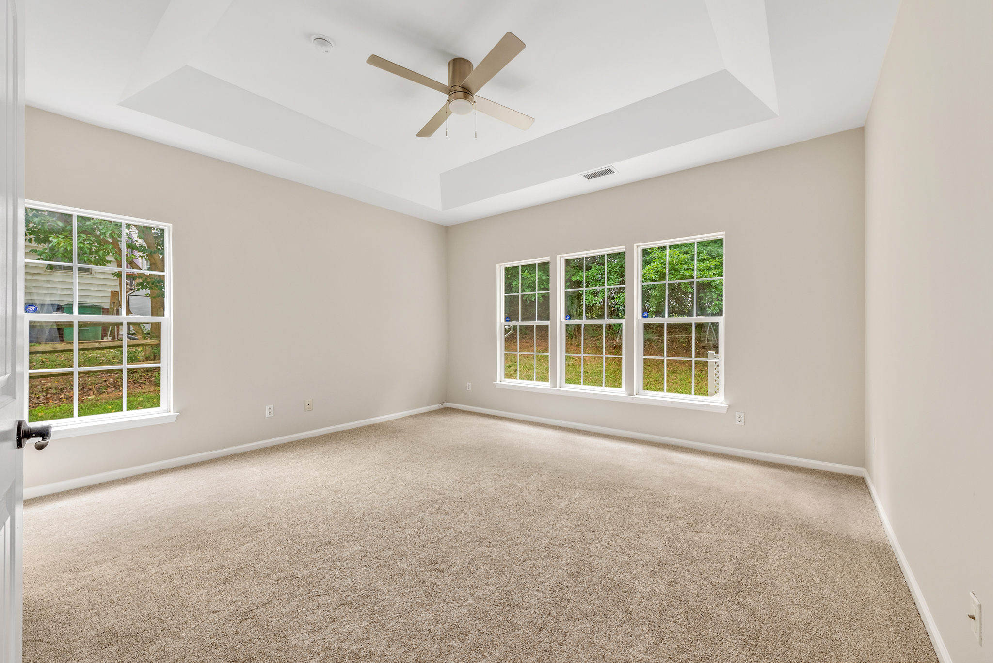 Vacant bedroom with tray ceiling and bright natural daylight from multiple windows