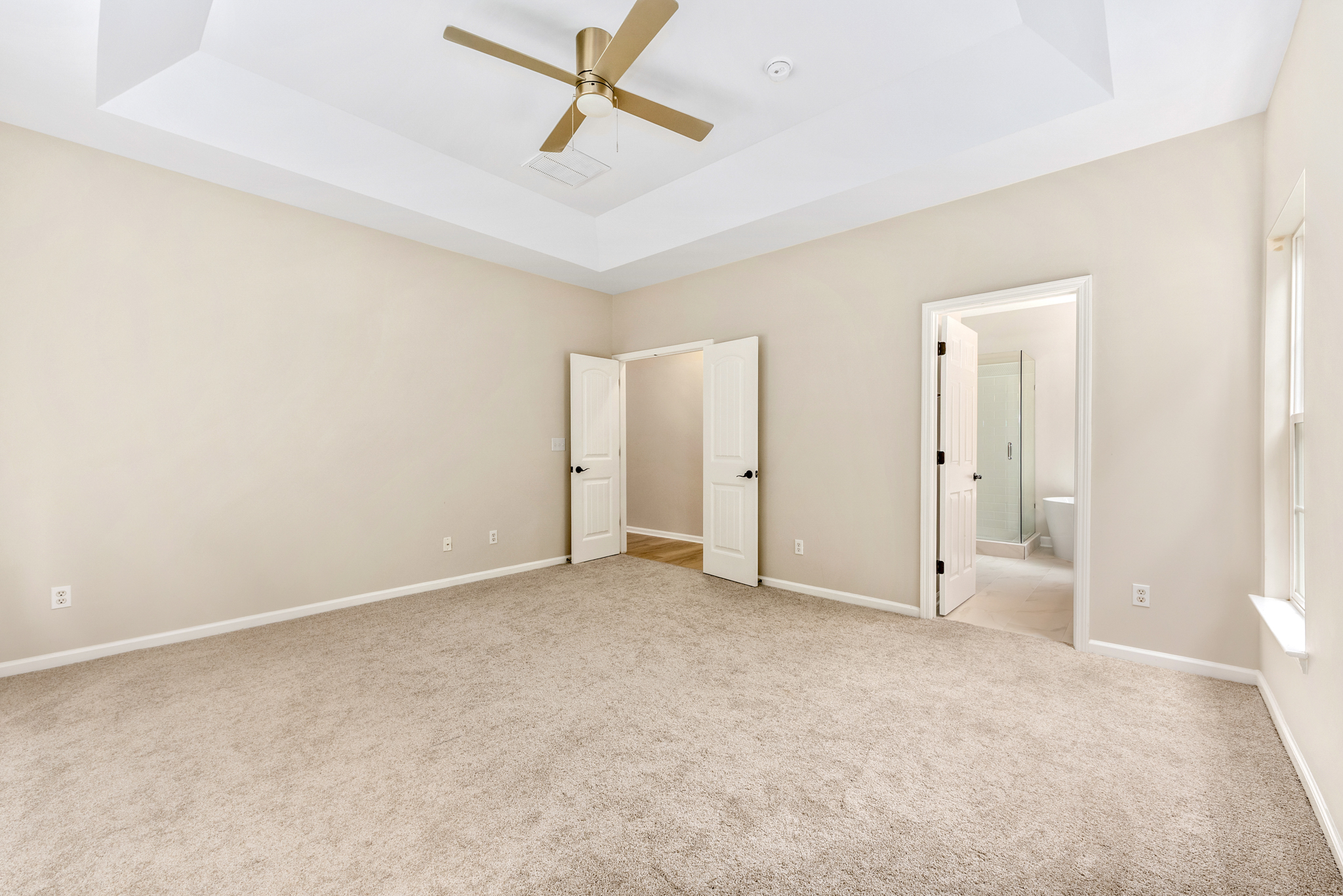Primary bedroom with tray ceiling and natural light