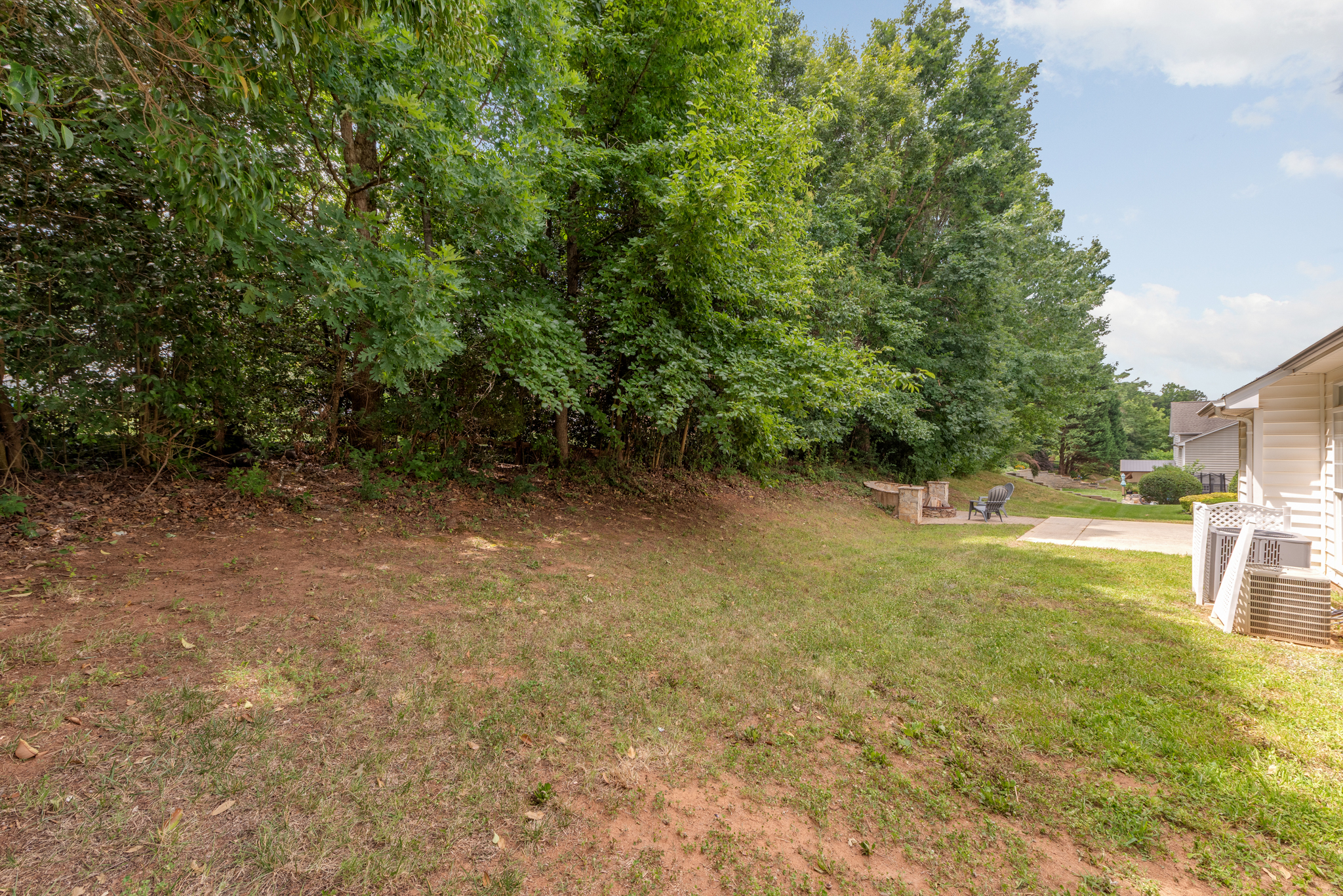 Backyard with flat lawn, stone firepit area, and mature tree canopy