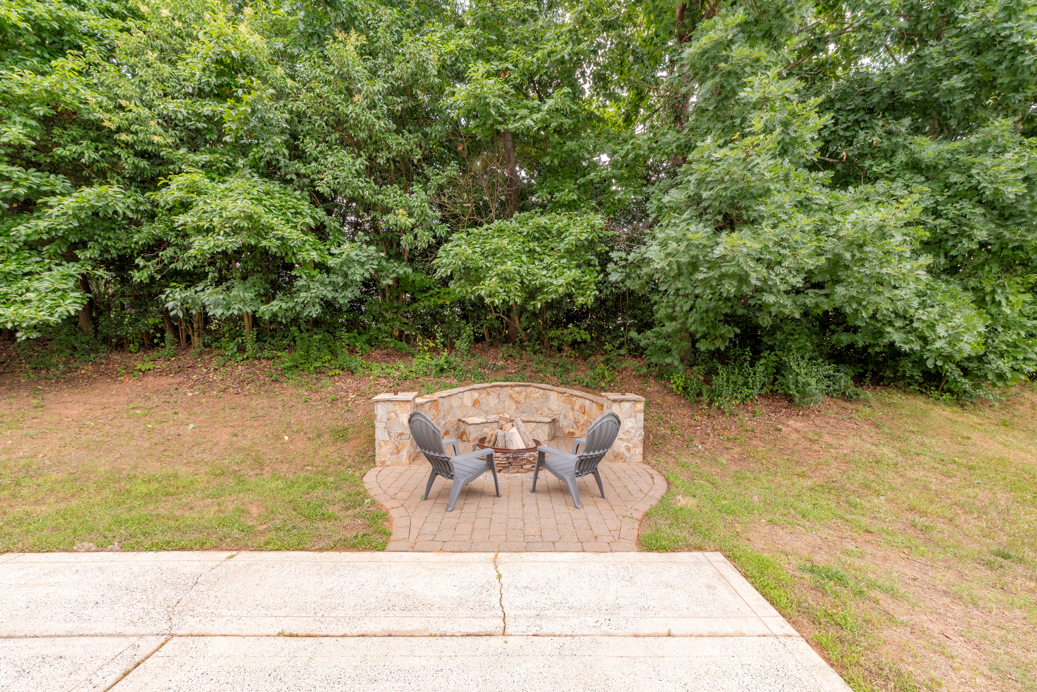 Stone firepit area with patio pavers bordered by mature trees