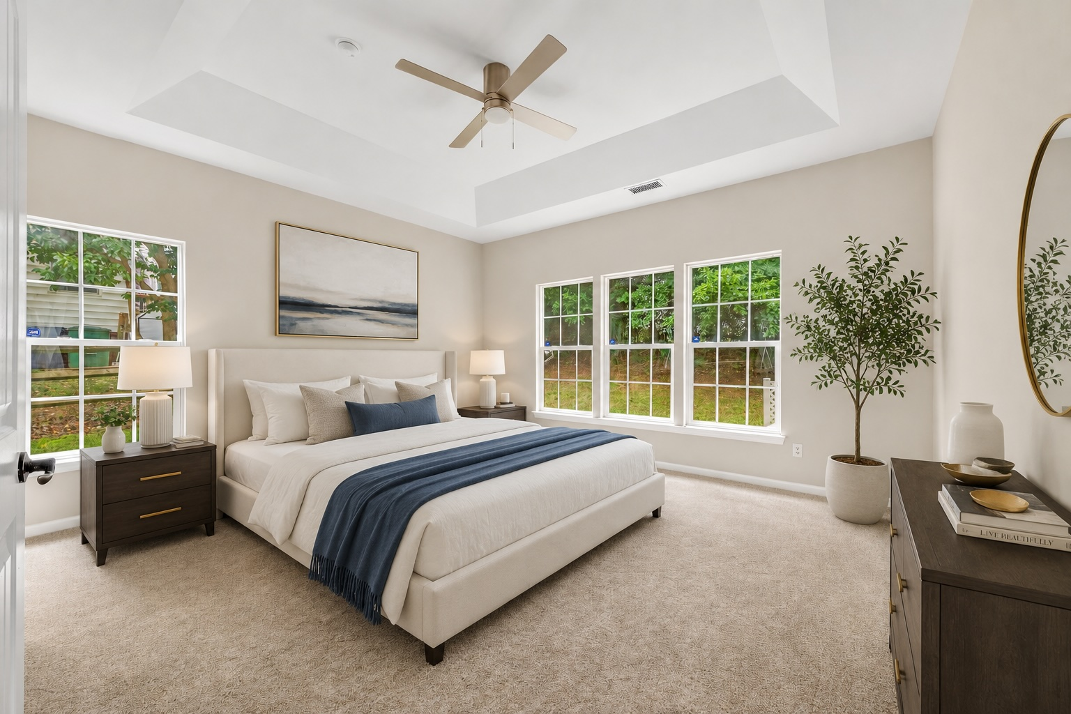 Furnished primary bedroom with tray ceiling, upholstered bed, and warm natural light