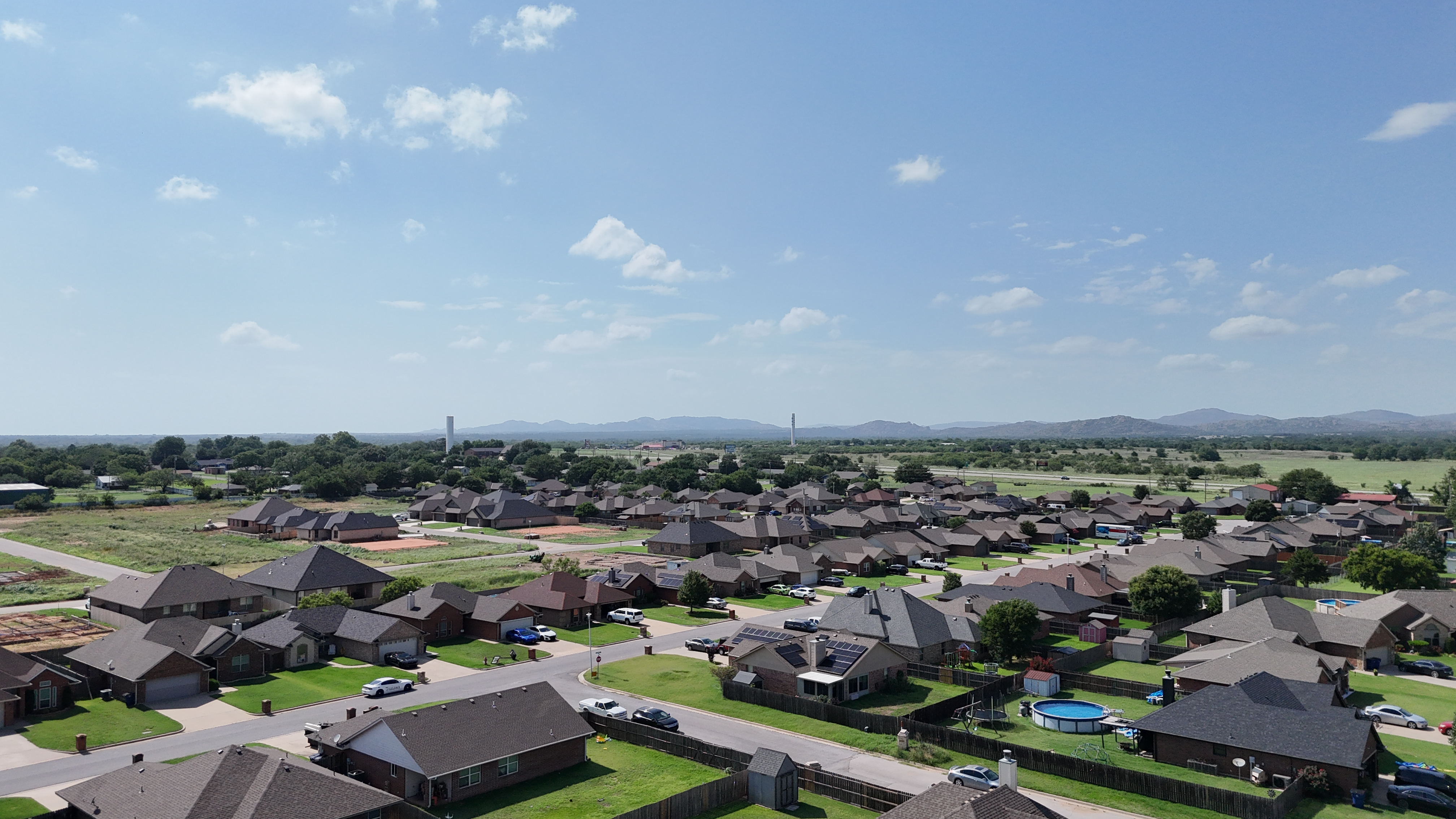 Aerial drone view of Cache, Oklahoma neighborhood with residential streets, open plains, and the Wichita Mountains in the distance