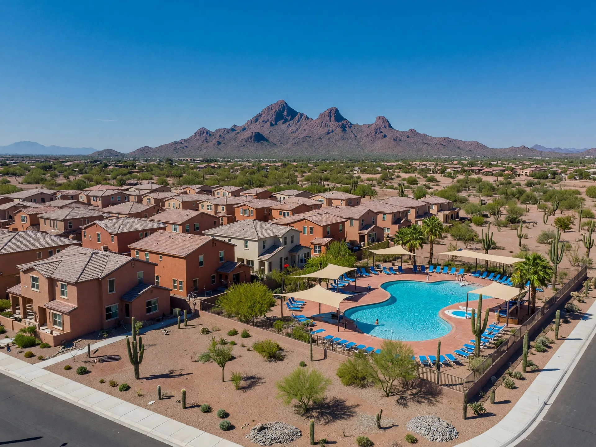 New construction master-planned community in Phoenix with earth-tone stucco homes, community pool, saguaro cacti, and Camelback Mountain in the background