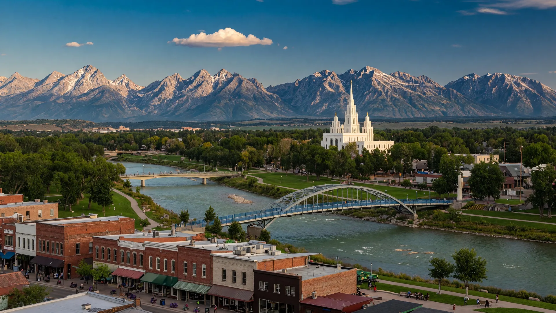 Downtown Idaho Falls along the Snake River Greenbelt with the Idaho Falls Temple and the Teton Mountain Range visible in the distance on a clear afternoon