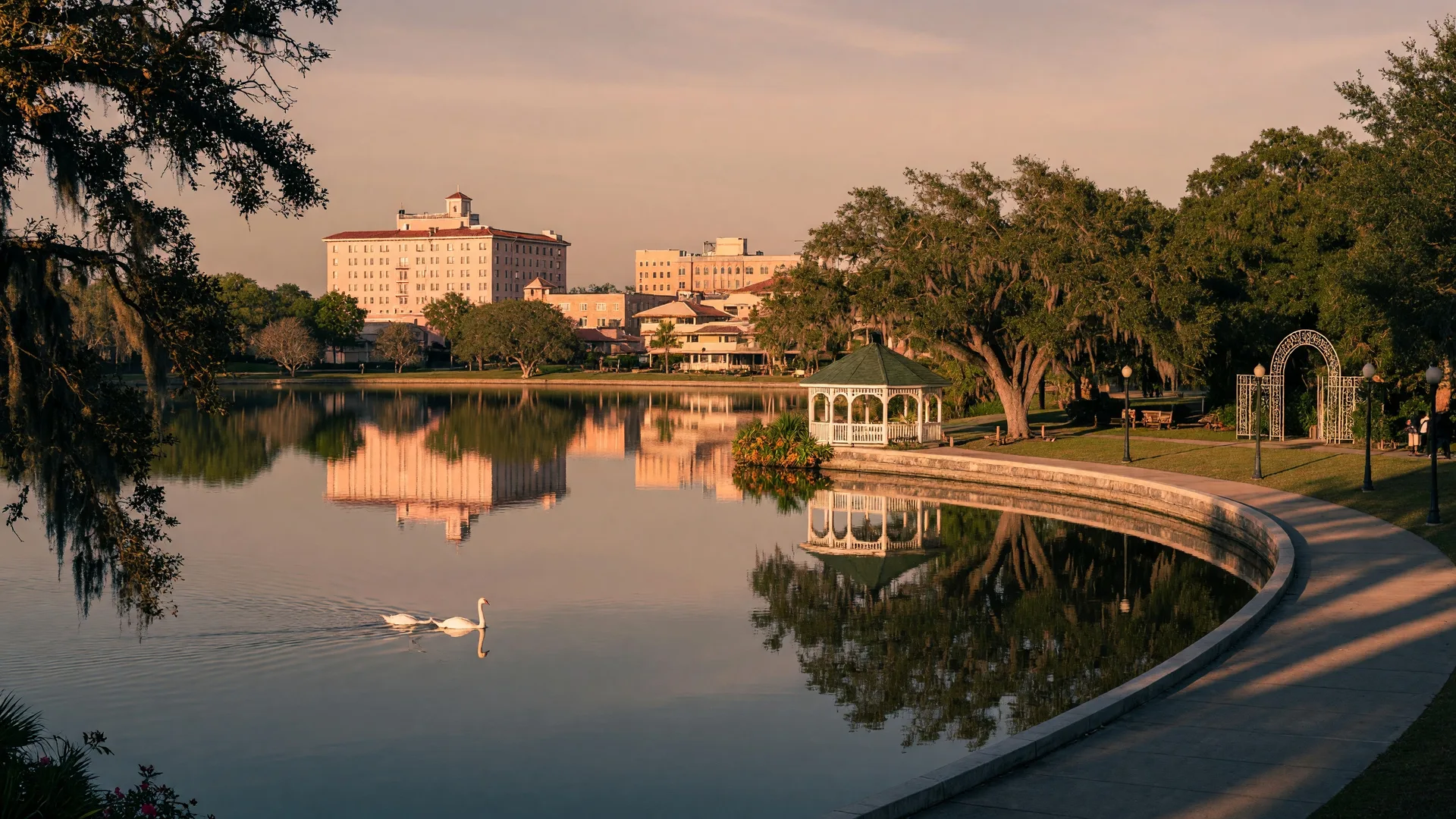 Downtown Lakeland skyline reflected in Lake Mirror with the historic Promenade, Hollis Garden, and swans on the lake at golden hour