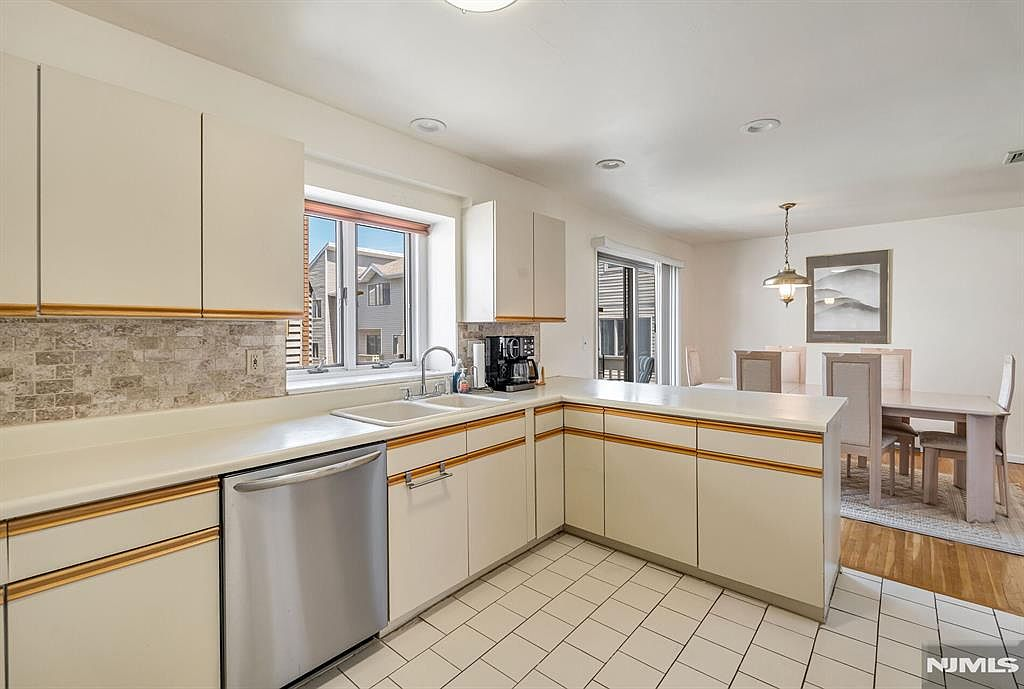 Kitchen with white cabinetry, stone mosaic backsplash, and open view to dining area
