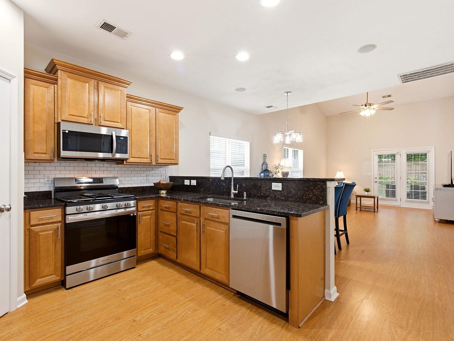 Open kitchen with granite countertops, stainless appliances, and view into the vaulted great room