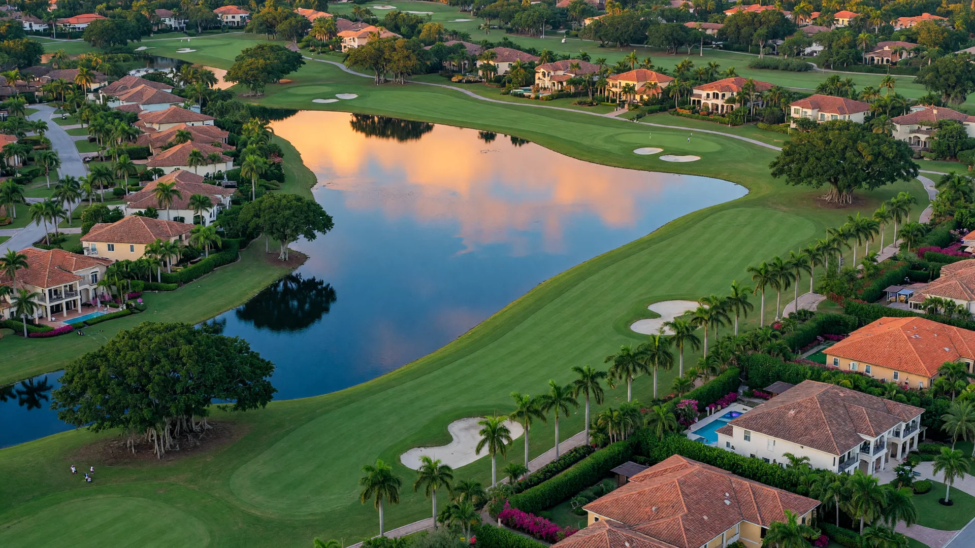 Luxury golf clubhouse in Naples Florida with Mediterranean architecture, tropical landscaping, and warm sunset lighting