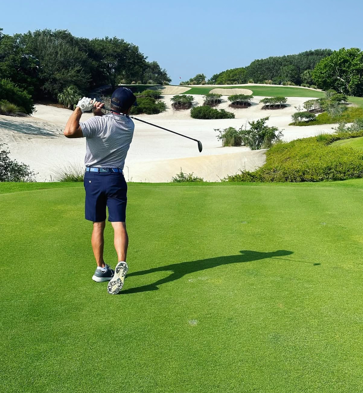 Alex Haigh golfing at Jupiter Hills — follow-through shot with dramatic sand bunkers