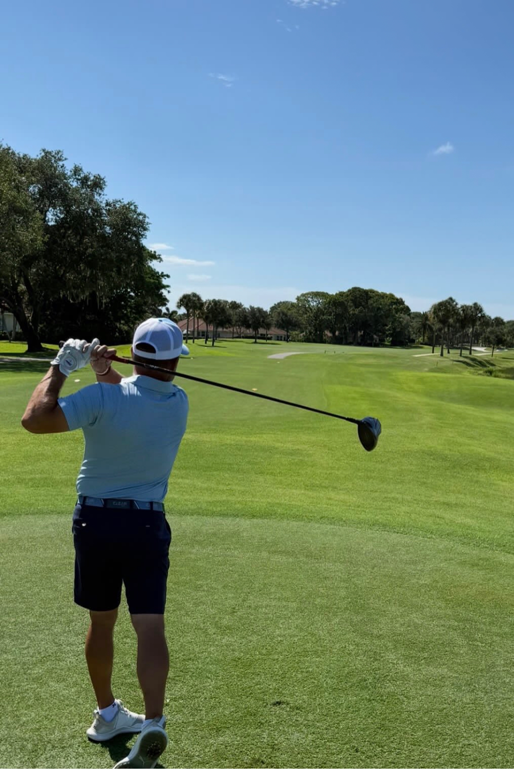 Alex Haigh at Mariner Sands — follow-through shot from behind on a green fairway with palm trees
