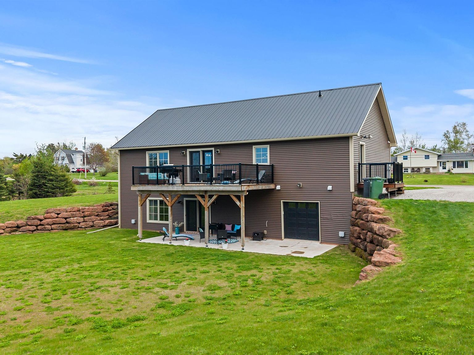 Backyard view of 74 Richard Douglas Dr showing the elevated deck, walk-out lower level, and stone retaining walls