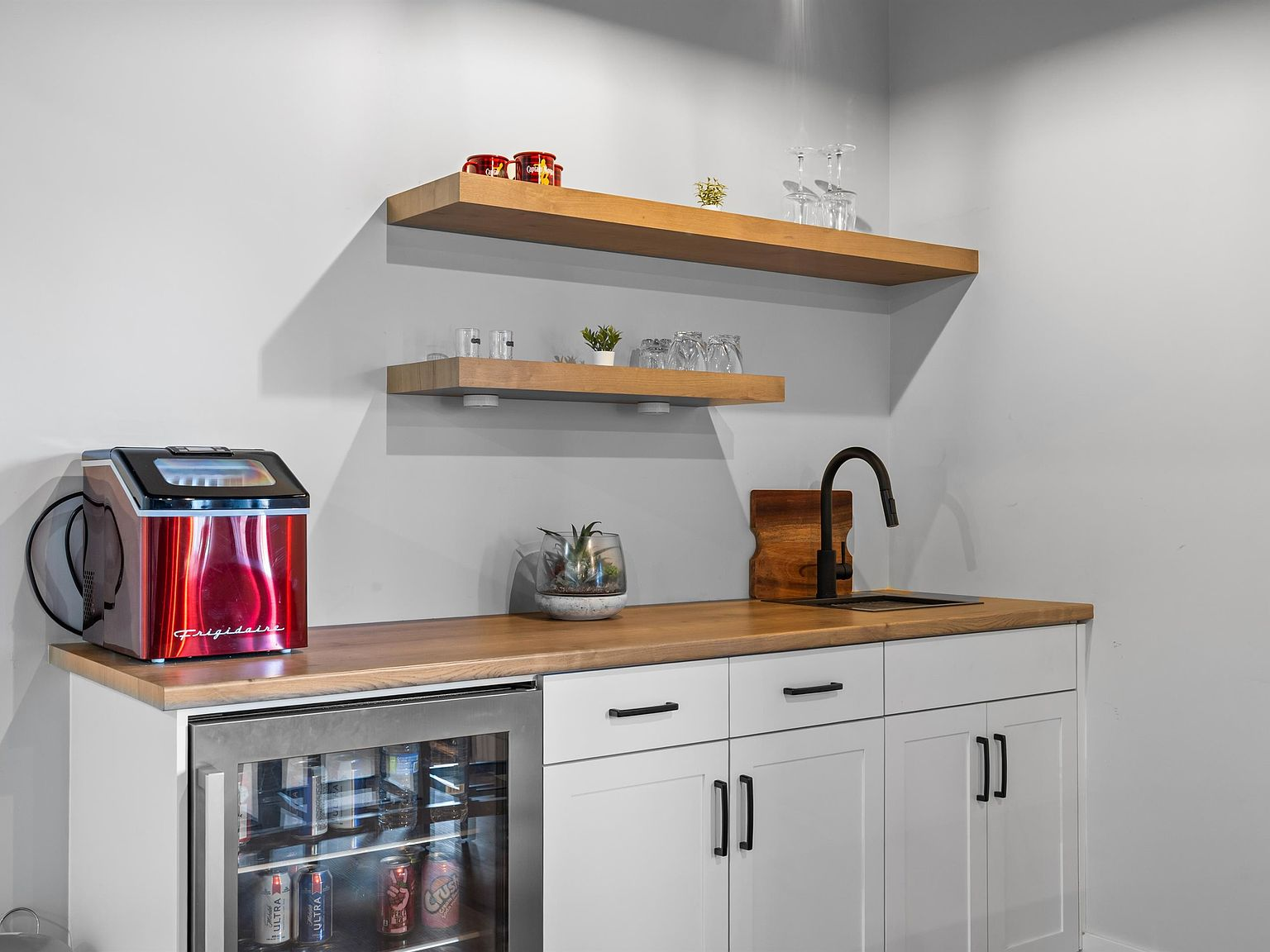 Lower level wet bar with white shaker cabinets, butcher-block countertop, and floating shelves