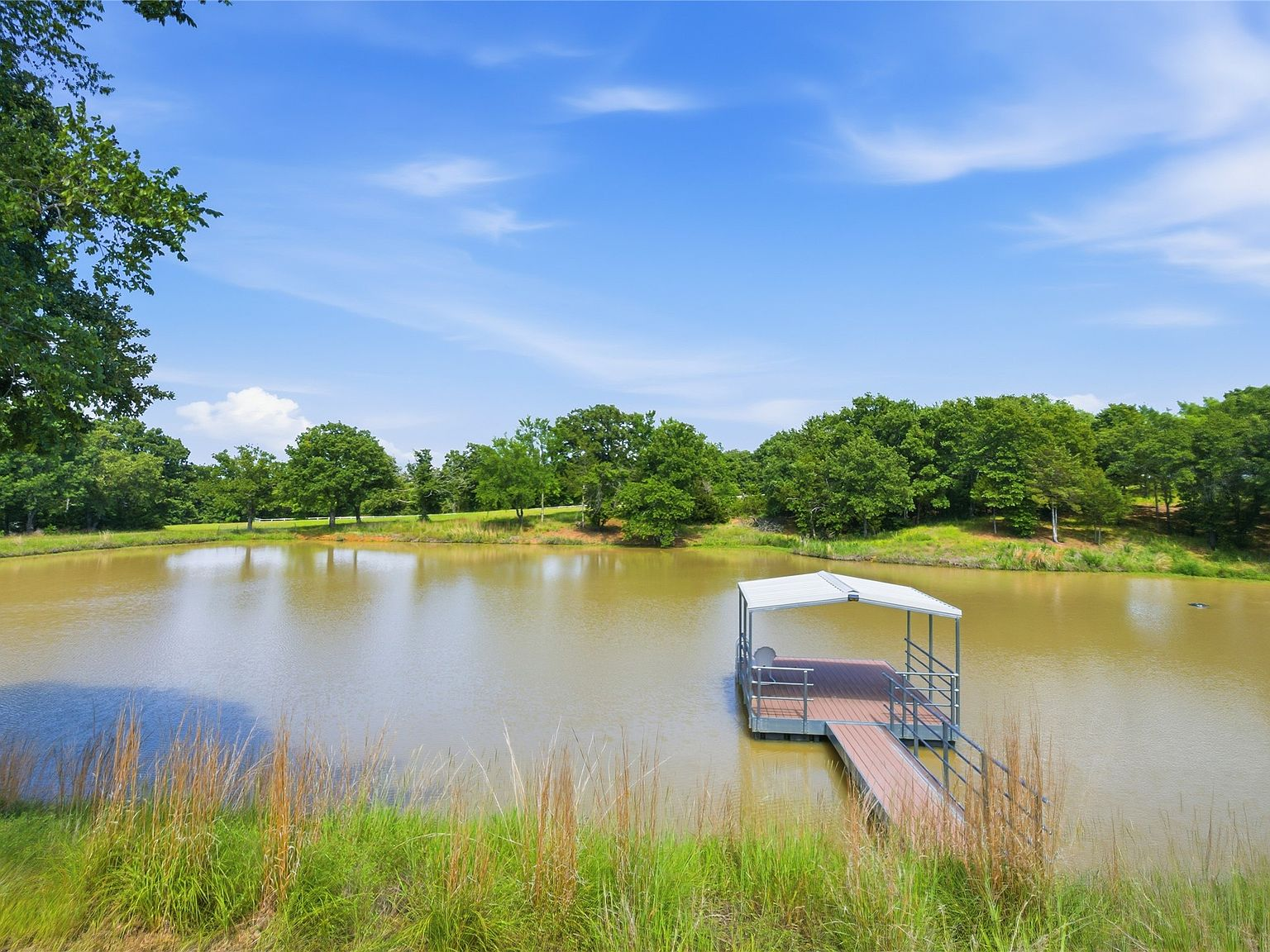 Private pond with covered dock, surrounded by mature oaks and rolling green hills