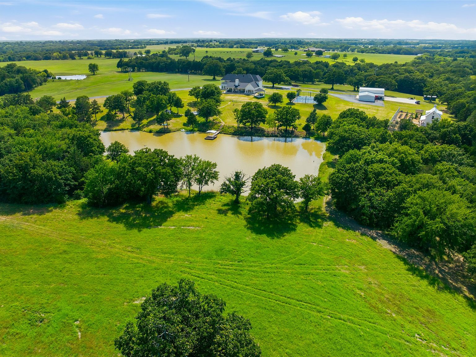 Aerial view of estate with large private pond, green pastures, and mature oak trees