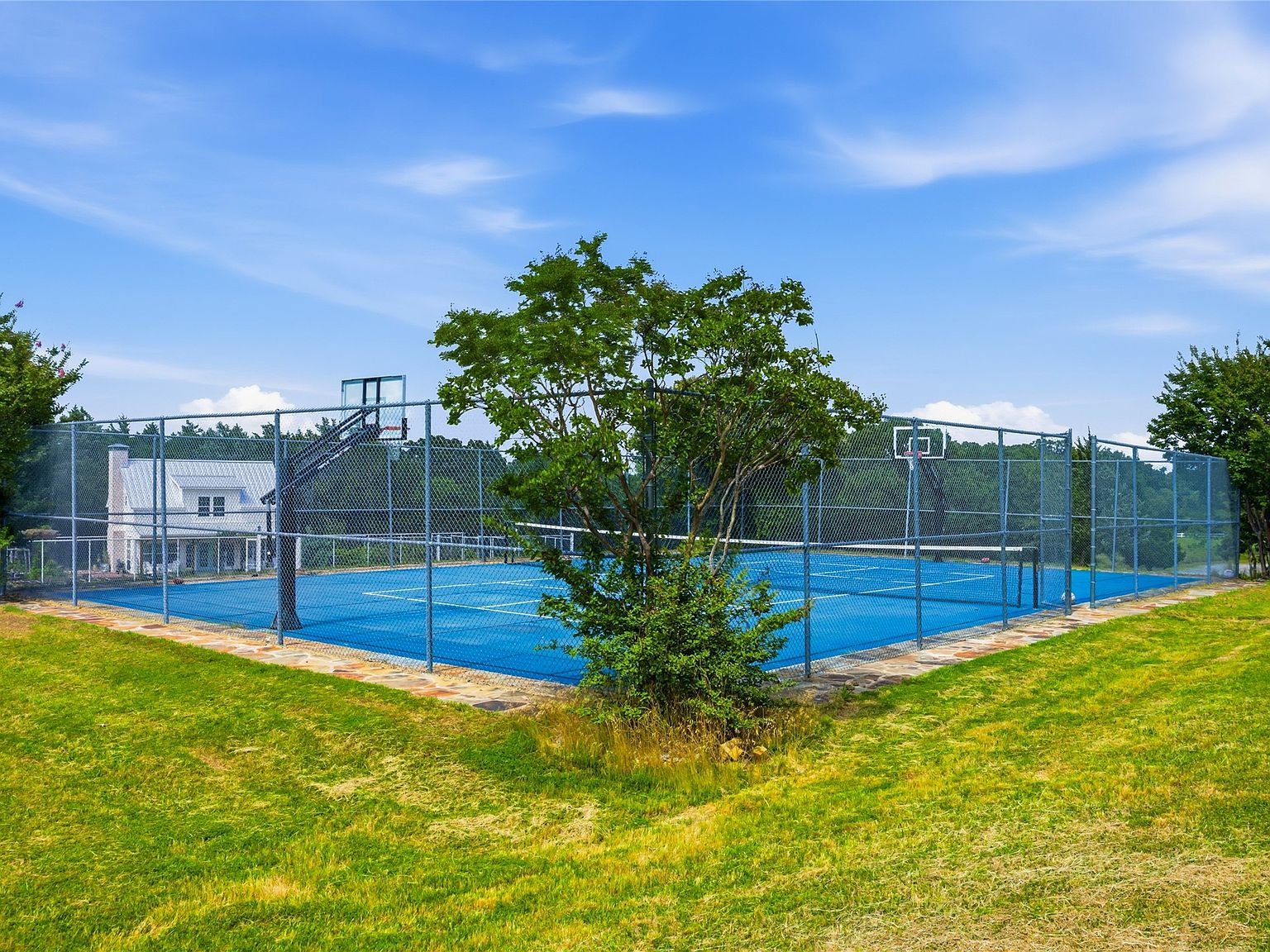 Fenced blue hard-surface tennis court with basketball hoops