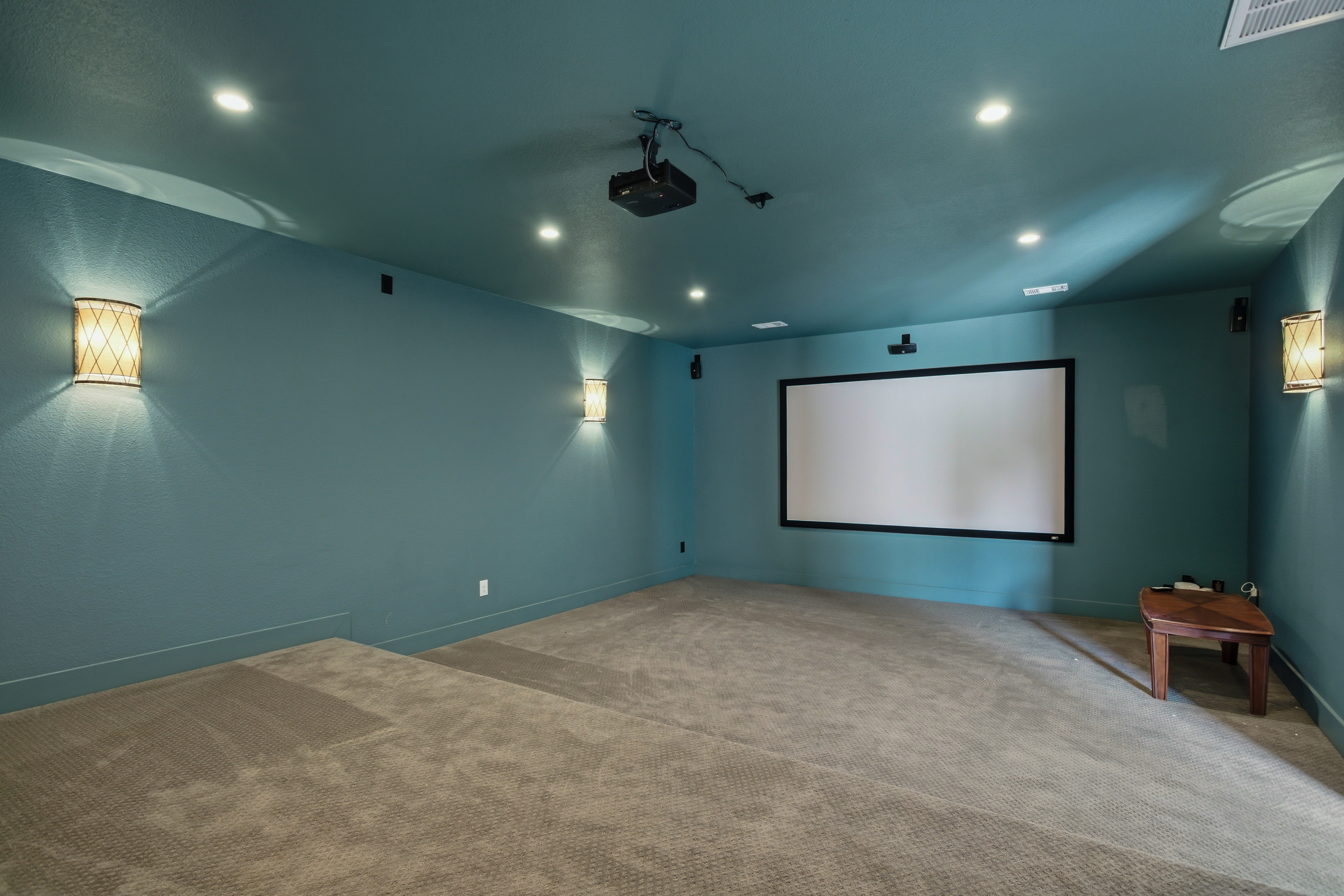 Dedicated media room with teal walls, tiered seating, and projector