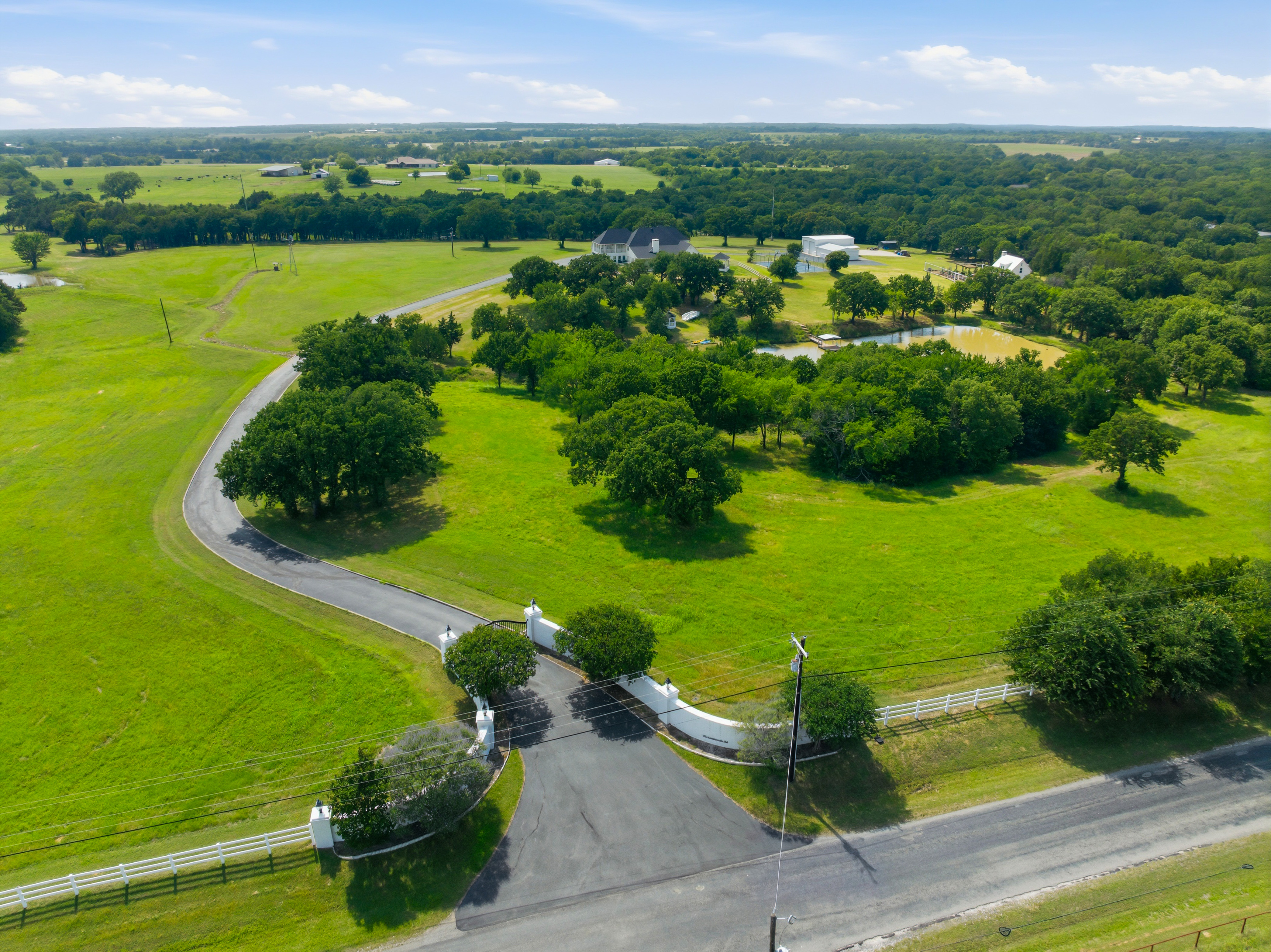Aerial view showing the entrance gate, winding driveway, pond, and all structures