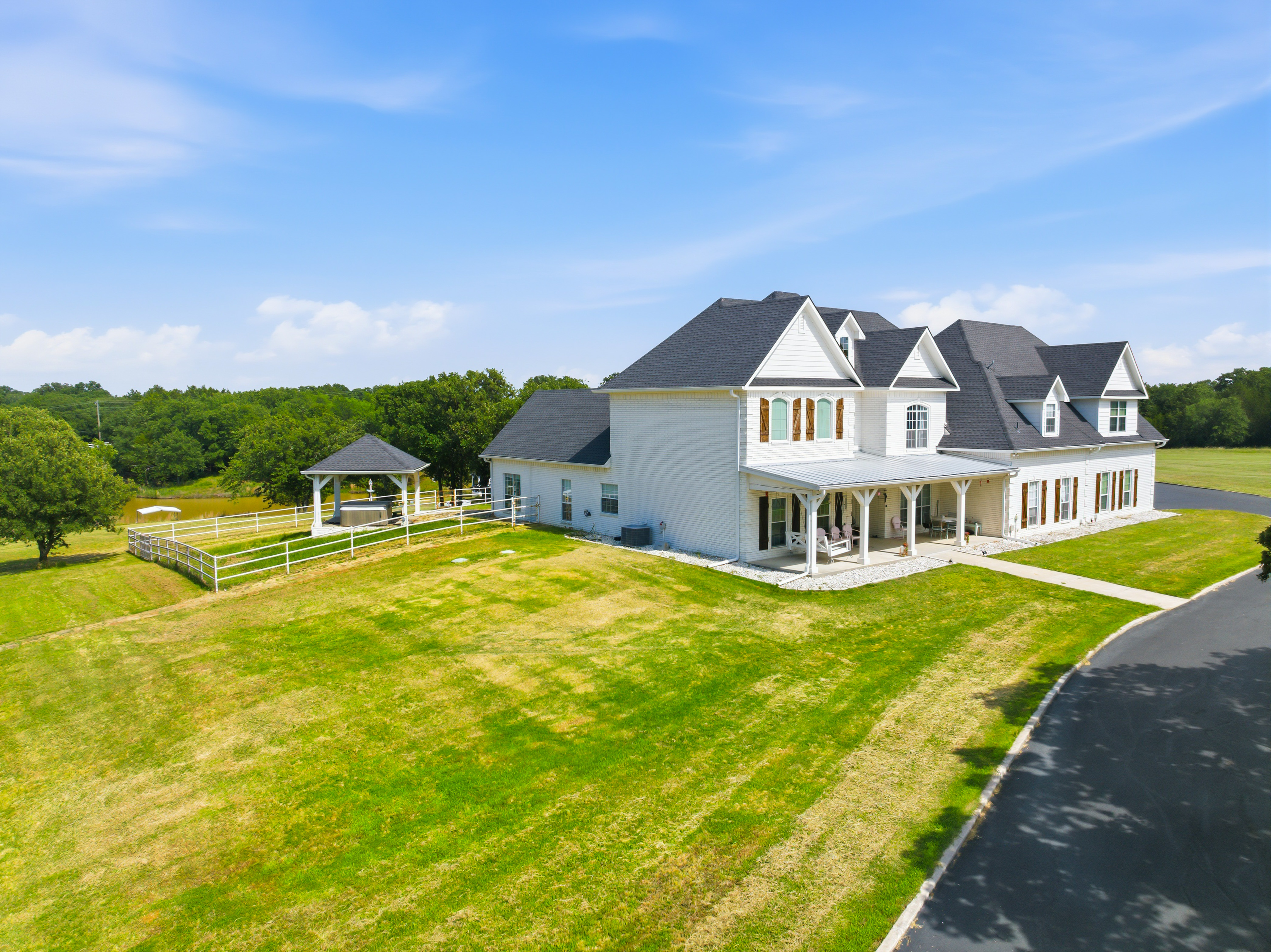 Aerial view of the estate with white brick, black gabled roof, and deep covered porch