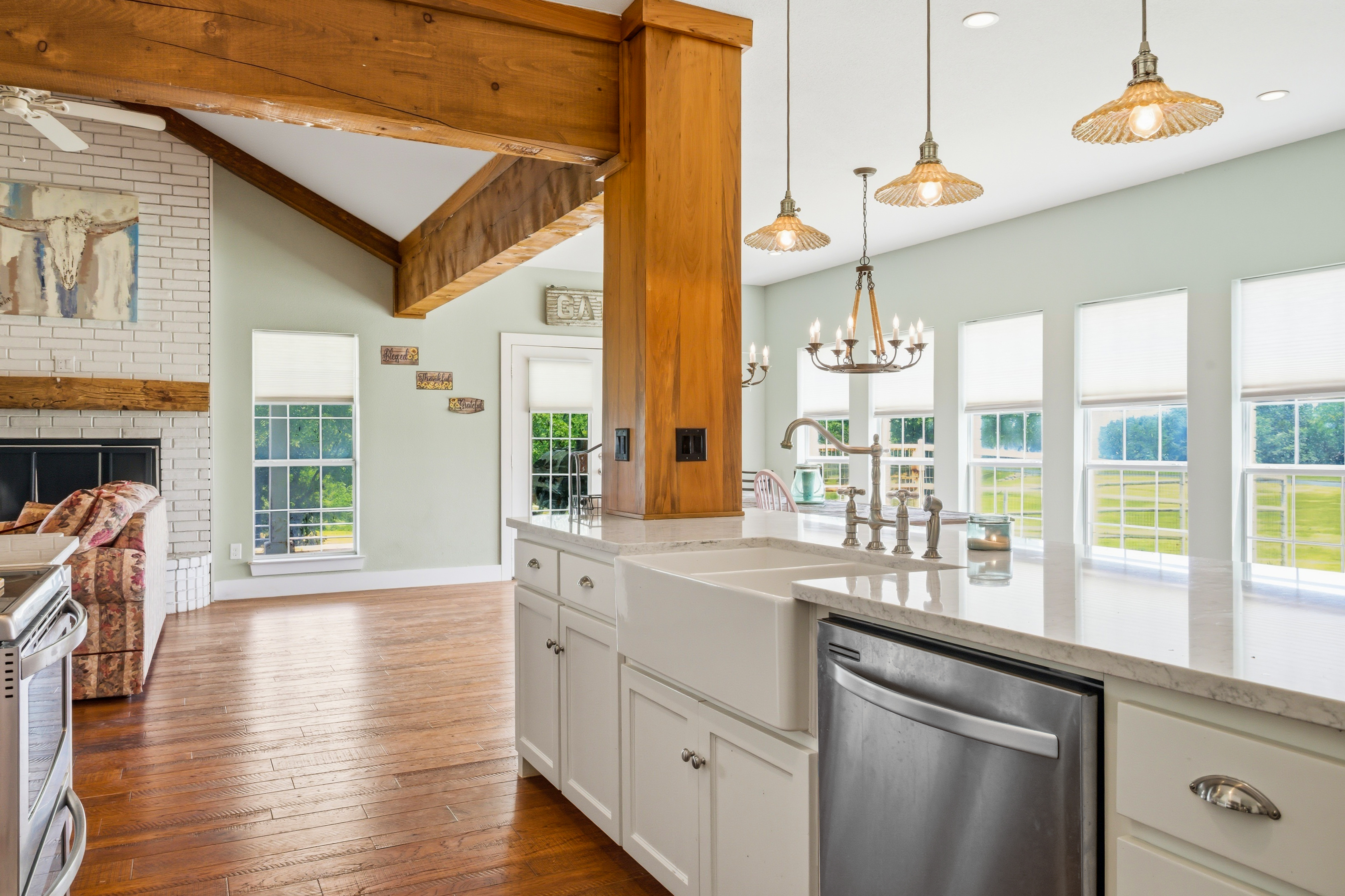 Open-concept kitchen and living area with farmhouse sink, quartz counters, and fireplace view