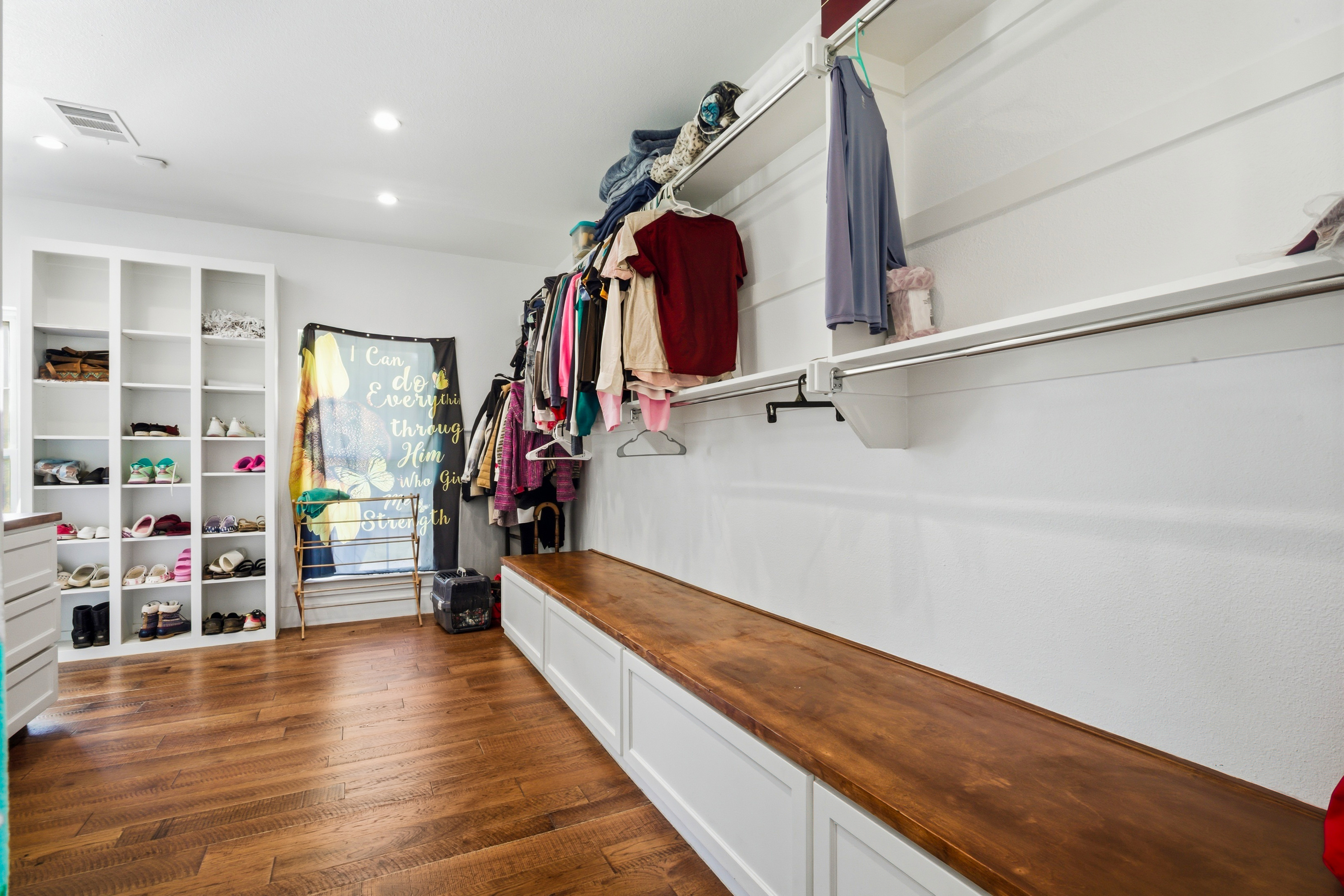 Walk-in closet with custom white cabinetry and hardwood bench top