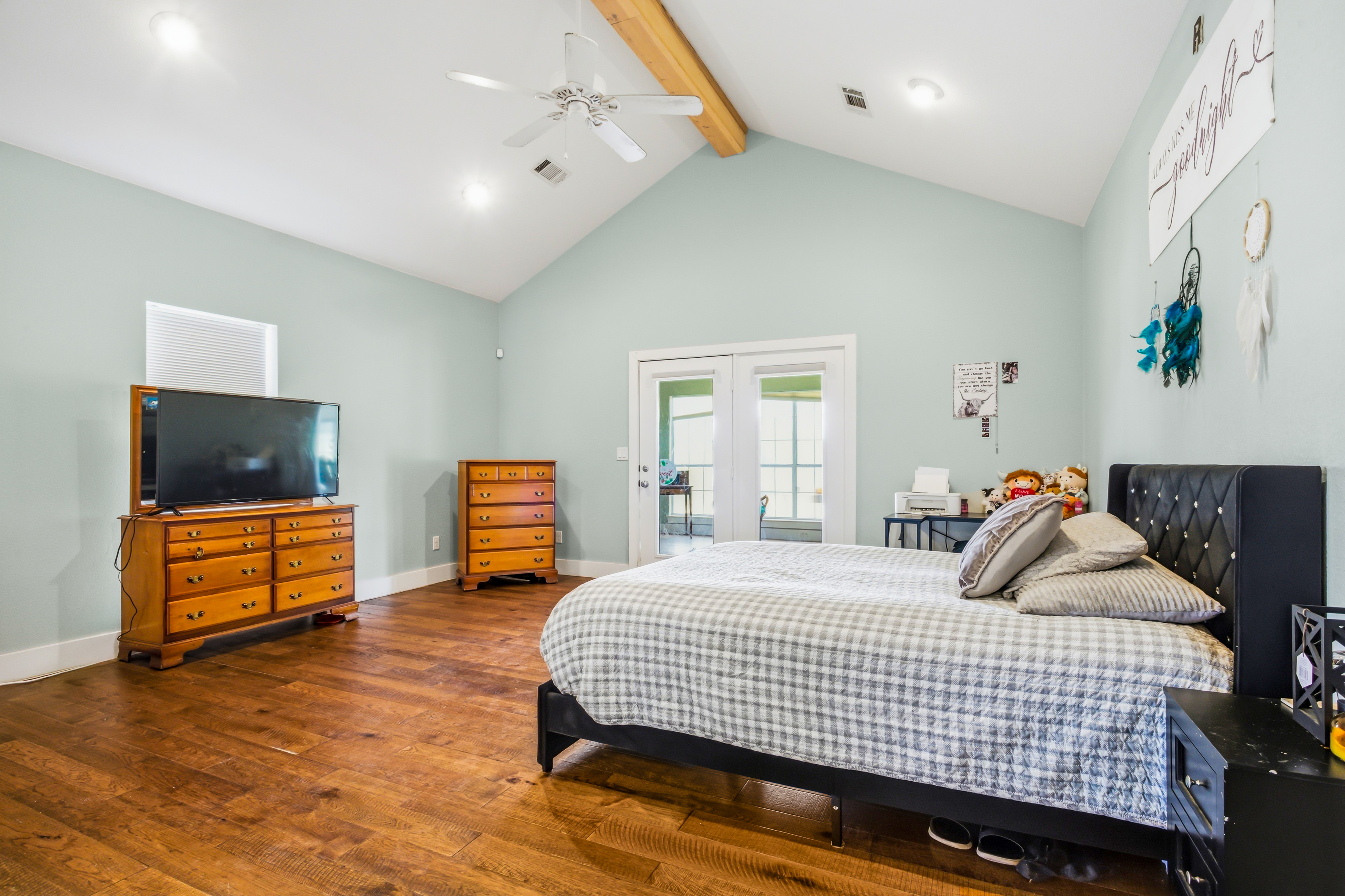 Primary suite bedroom with vaulted ceiling and wood beam, opening to sunroom