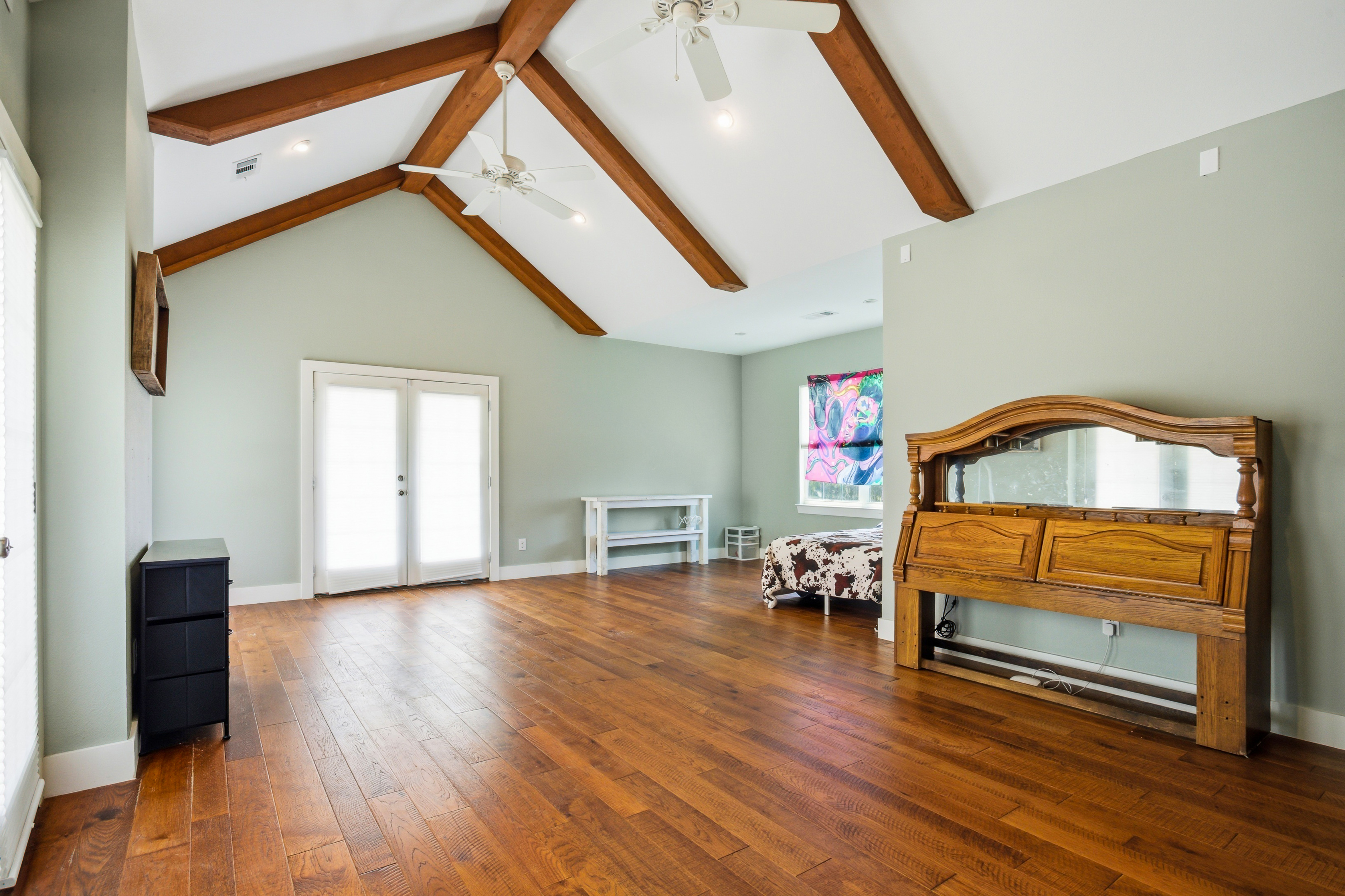 Primary bedroom with vaulted ceiling, exposed wooden beams, and dual French doors