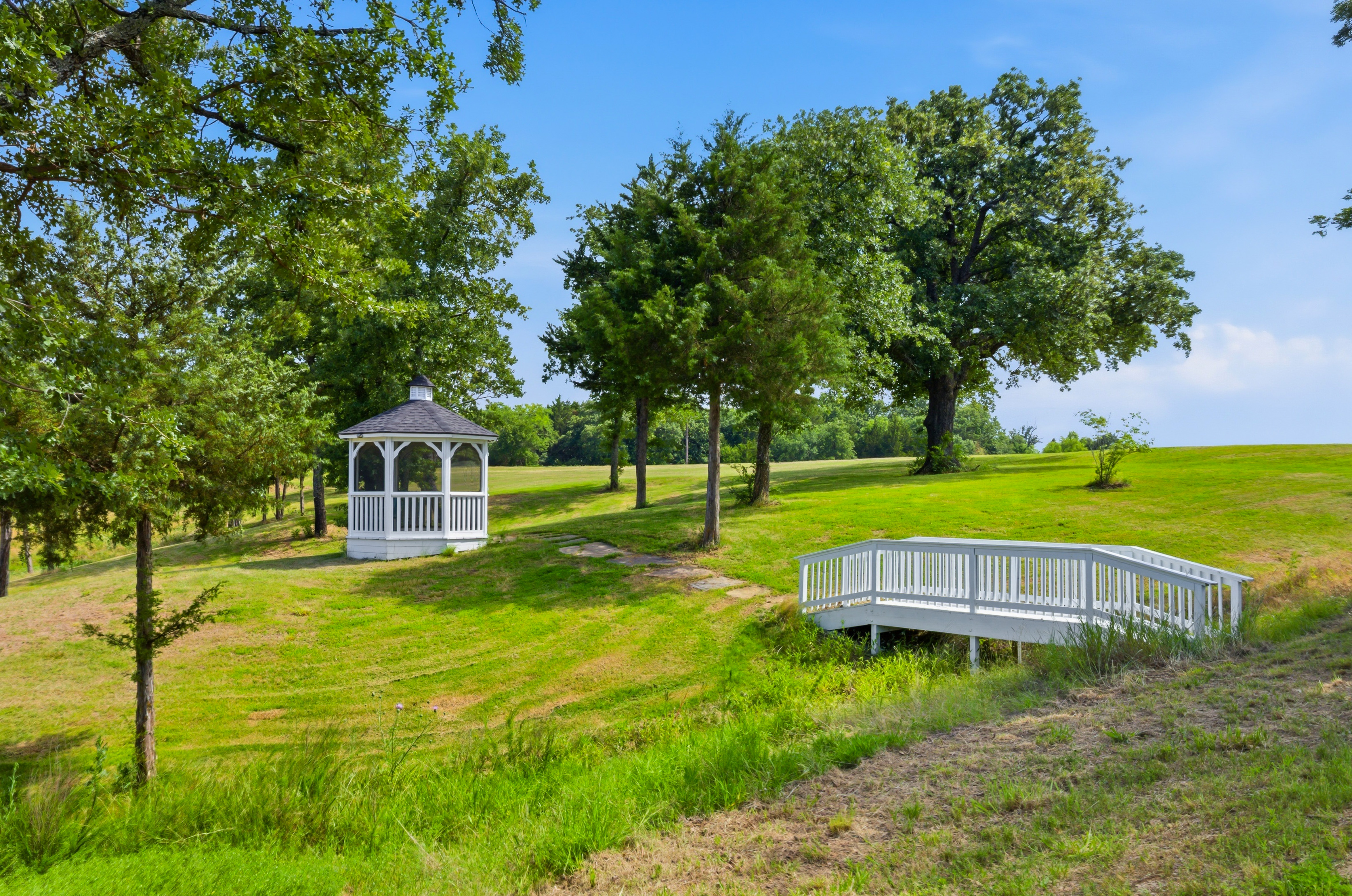 White wooden footbridge and gazebo with rolling green hills beyond