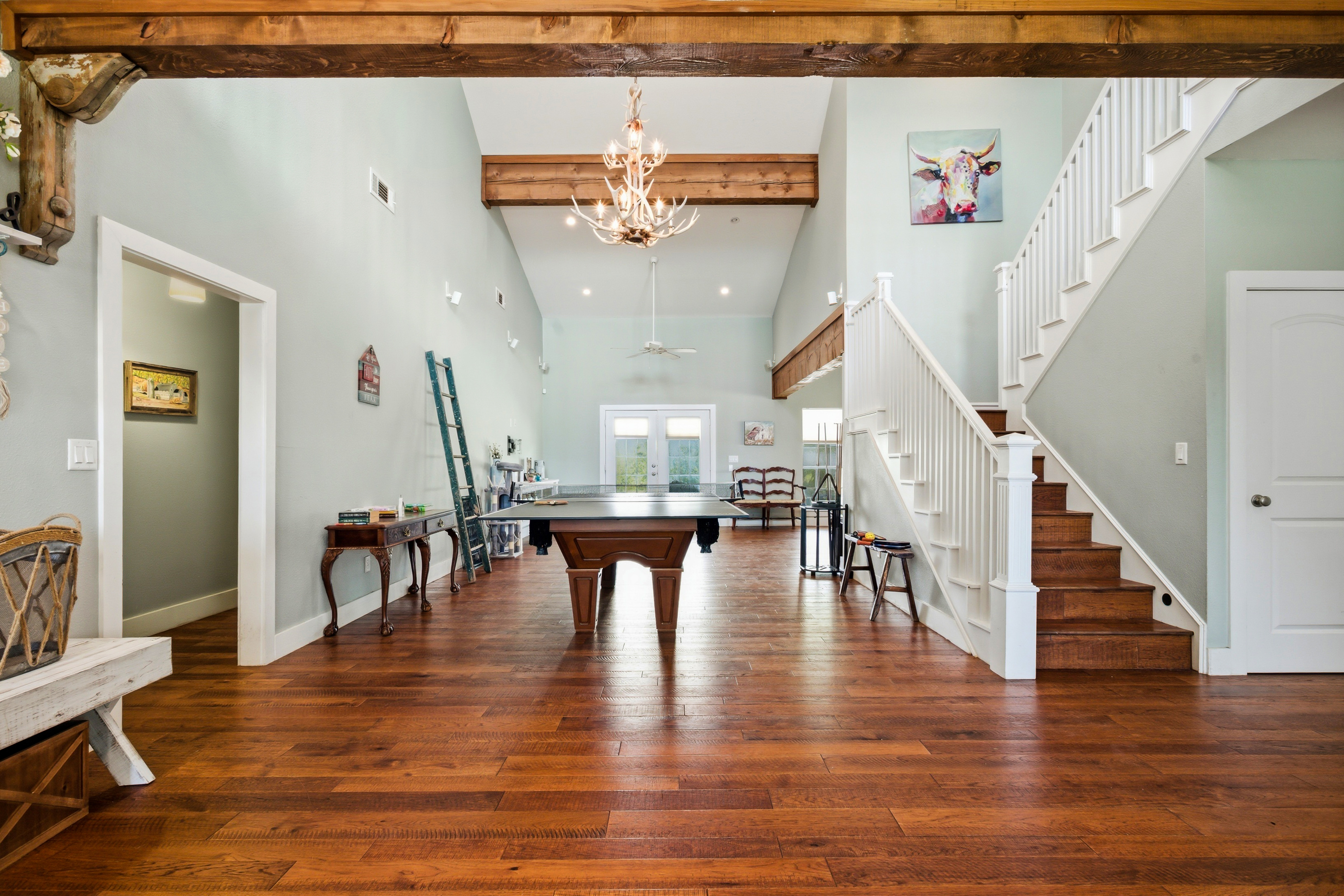 Grand entry living room with exposed pine ceiling beams, hardwood floors, and white-railed staircase, the dramatic first impression of the estate