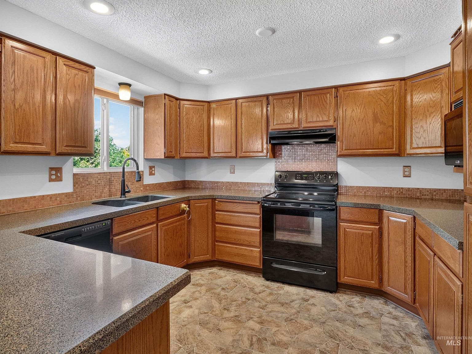 Updated kitchen with oak raised-panel cabinetry, mosaic tile backsplash, and black appliances
