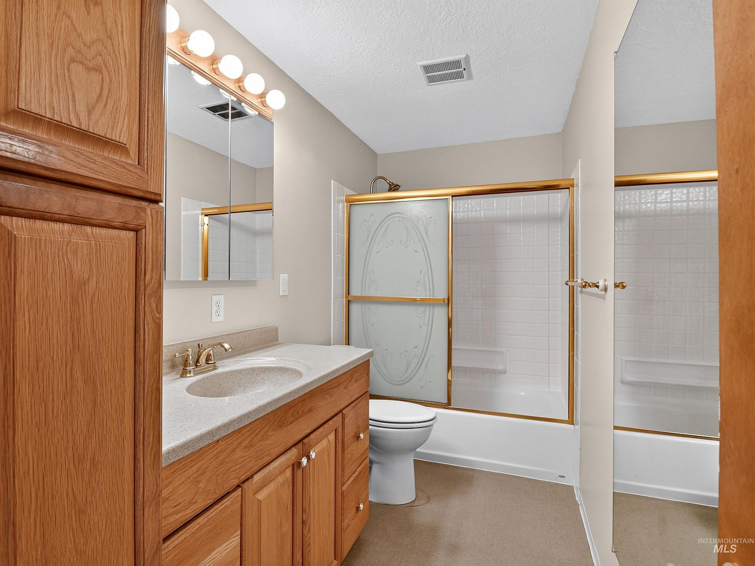 Bathroom with oak vanity, laminate countertop, and gold-trimmed shower