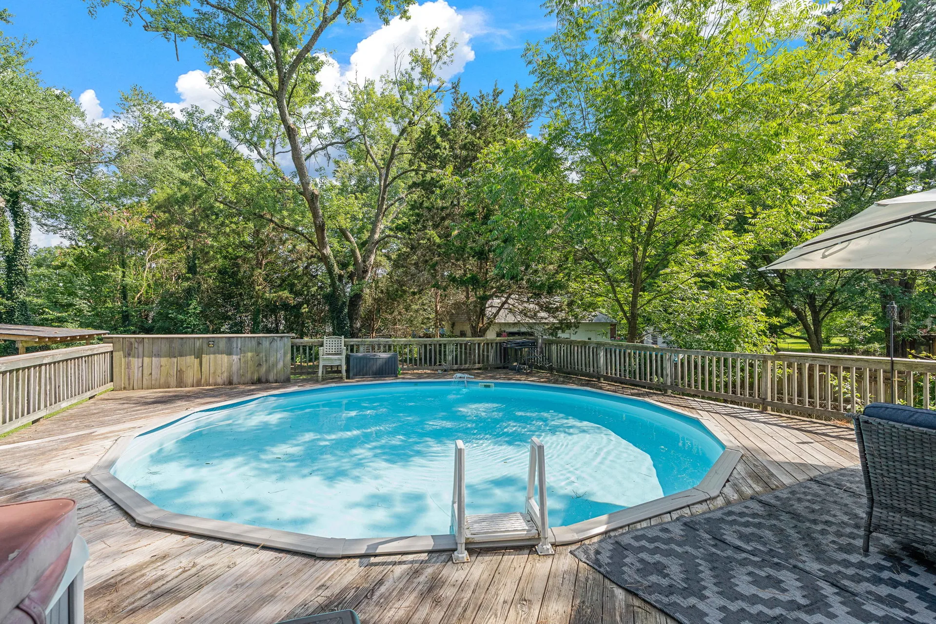 Above-ground pool with wrap-around wood decking and patio umbrella