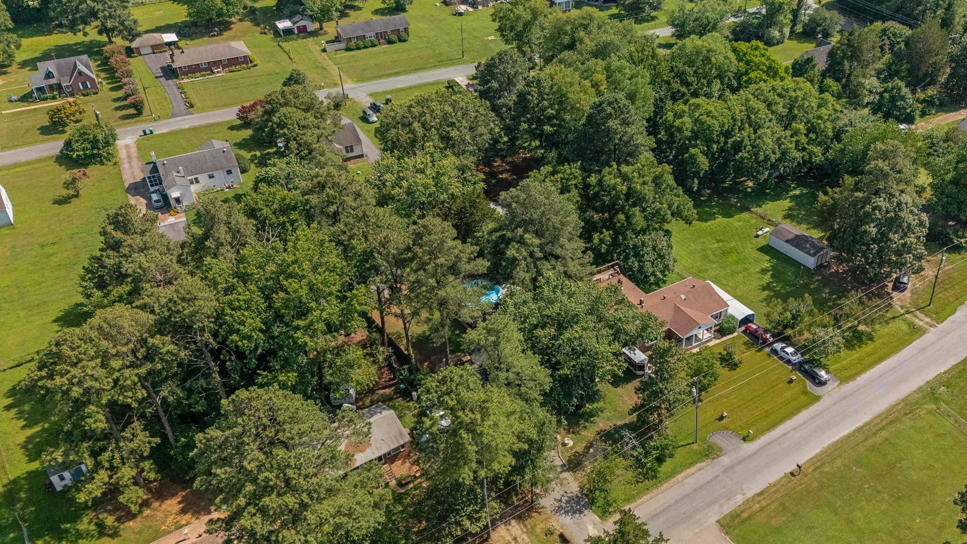 High-angle drone view showing pool, rear deck, and storage outbuilding