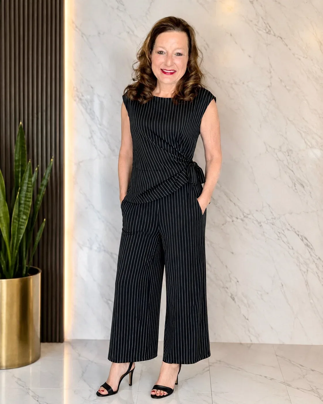 Kim Donahue in a black pinstripe jumpsuit, professional portrait in modern office