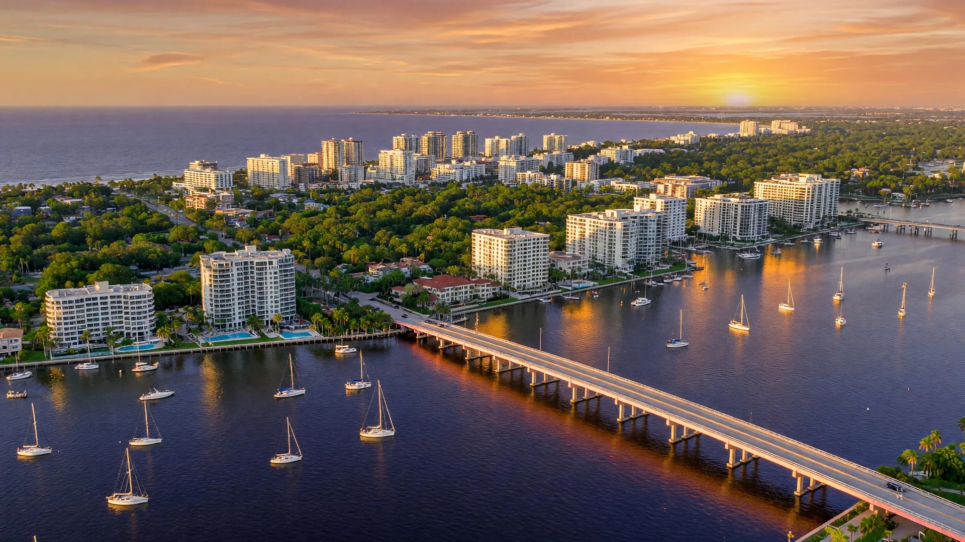 Modern waterfront condominium building in Sarasota Florida with a resort-style pool deck, glass balconies, tropical palm trees, and Sarasota Bay in the background