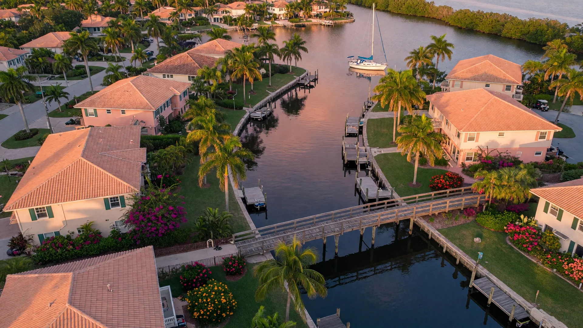Aerial drone view of a Sarasota coastal neighborhood at golden hour with waterfront homes, canals, and palm trees