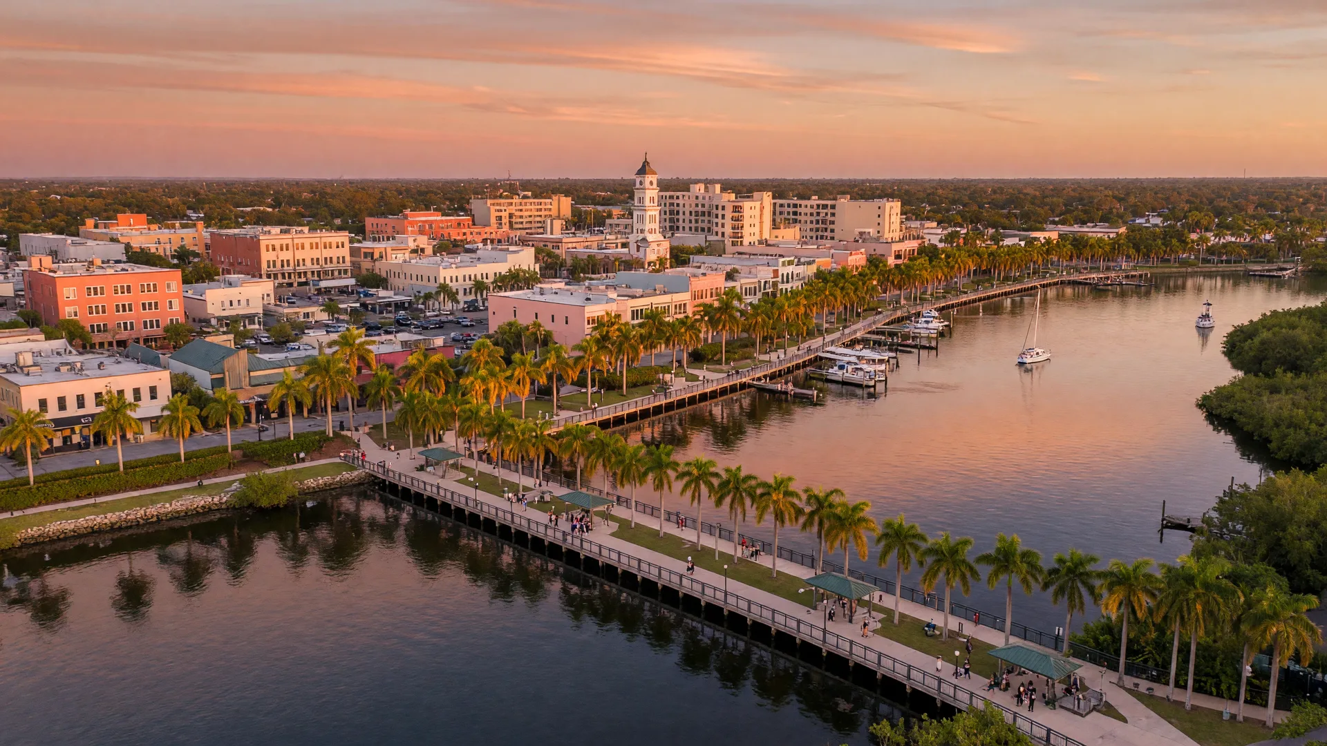 Downtown Bradenton waterfront along the Manatee River with the Riverwalk boardwalk, palm trees, and warm sunset light reflecting off calm water