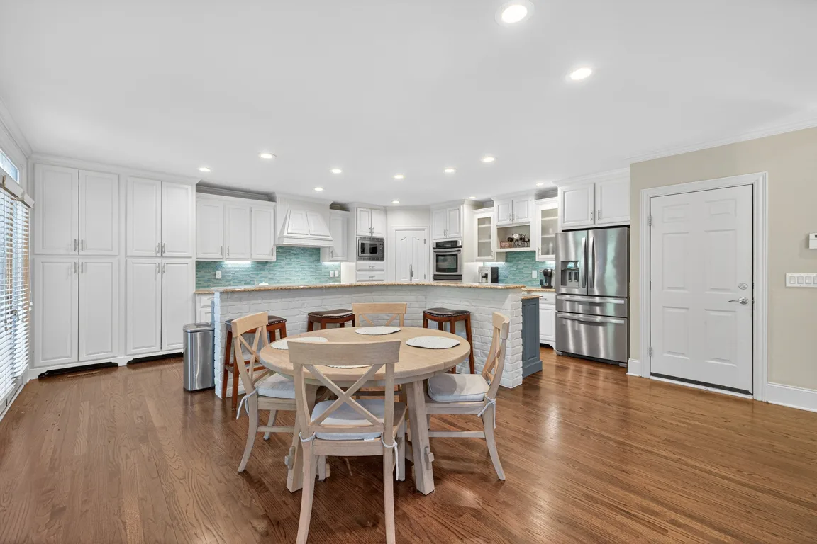 Chef's kitchen with white cabinets, blue island, teal glass tile backsplash, and granite countertops at 909 Pathview Court
