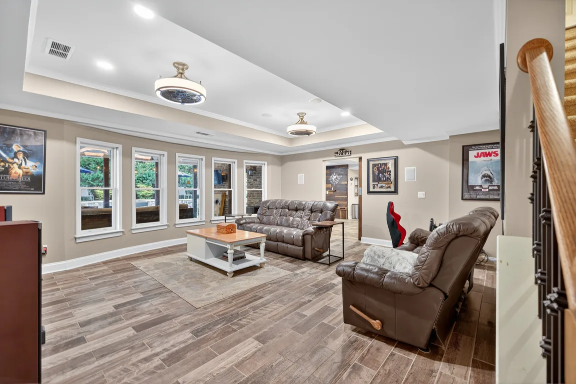 Finished terrace level lounge area with wood-plank accent wall, media setup, and tray ceiling at 909 Pathview Court