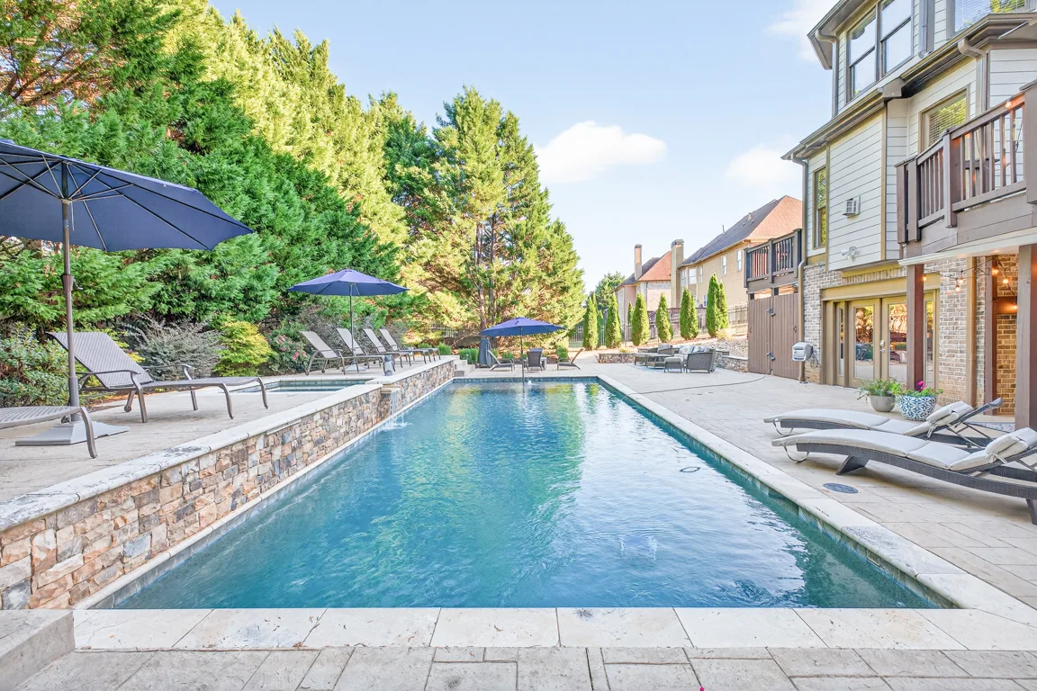 In-ground swimming pool with stone veneer house in background