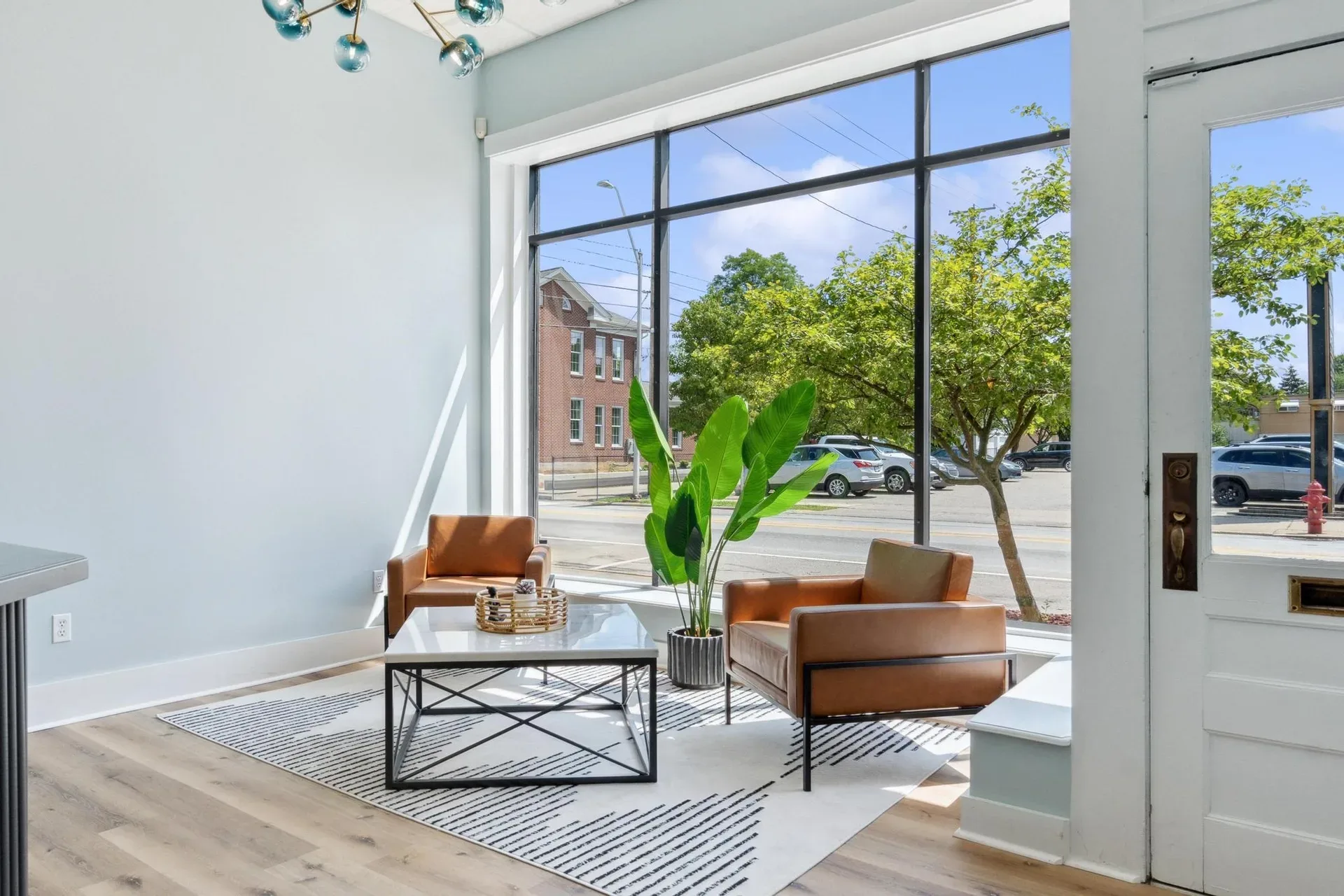 Bright office waiting area at Glasshouse Realty with light wood floors, two tan leather chairs, and a geometric rug near a large window in Wilmington, Ohio