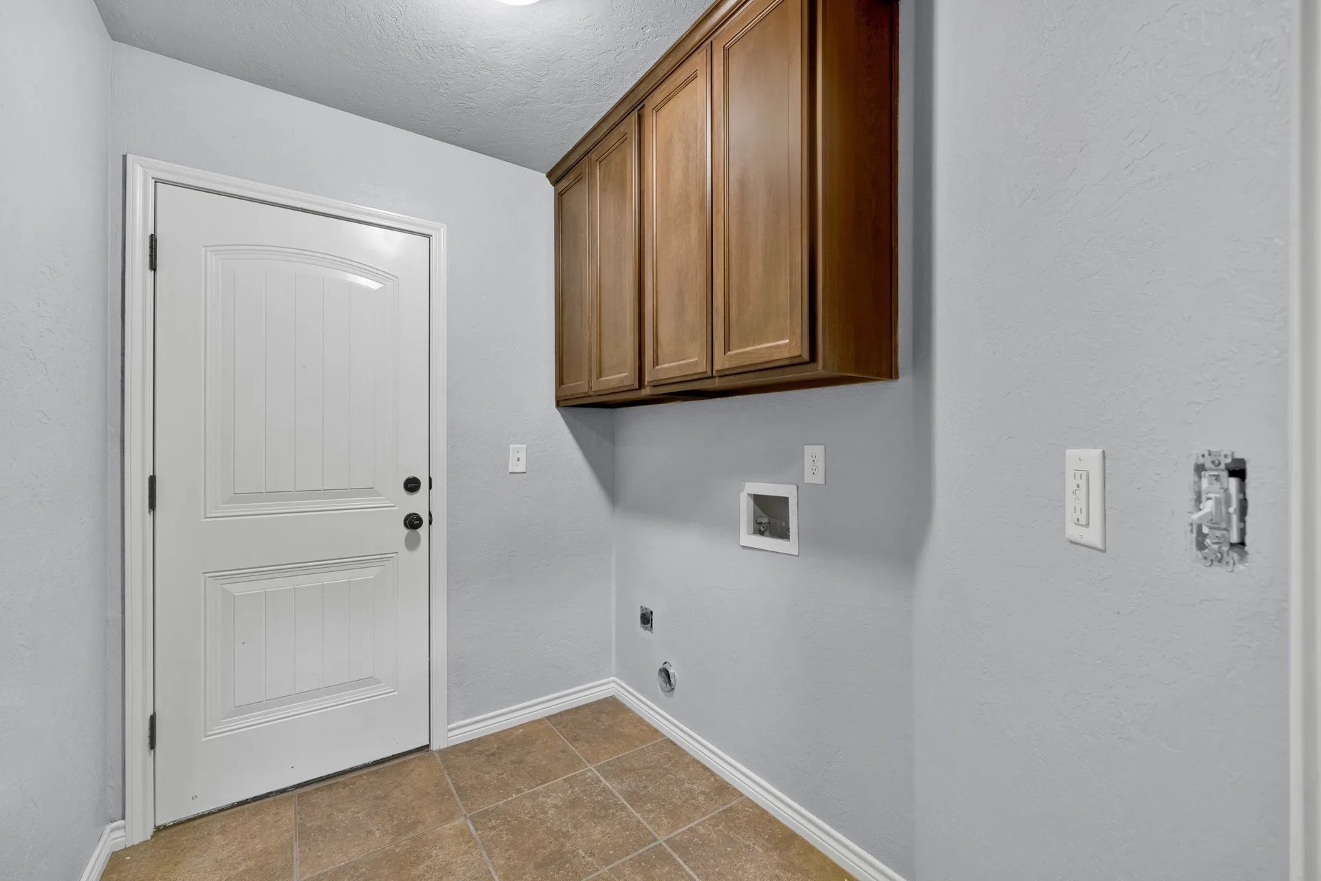 Utility laundry room with ceramic tile flooring and upper cabinets