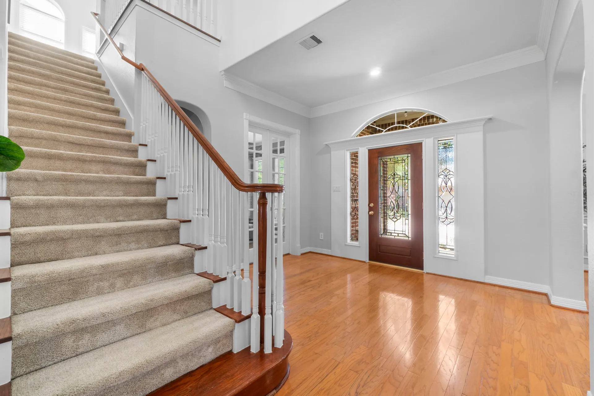 Foyer and entryway staircase with wood flooring, carpeted stairs, and wooden handrail