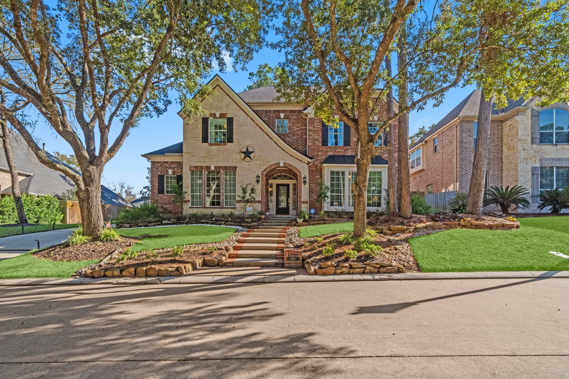 Street-level view of two-story brick home with stone veneer accents and dark shutters